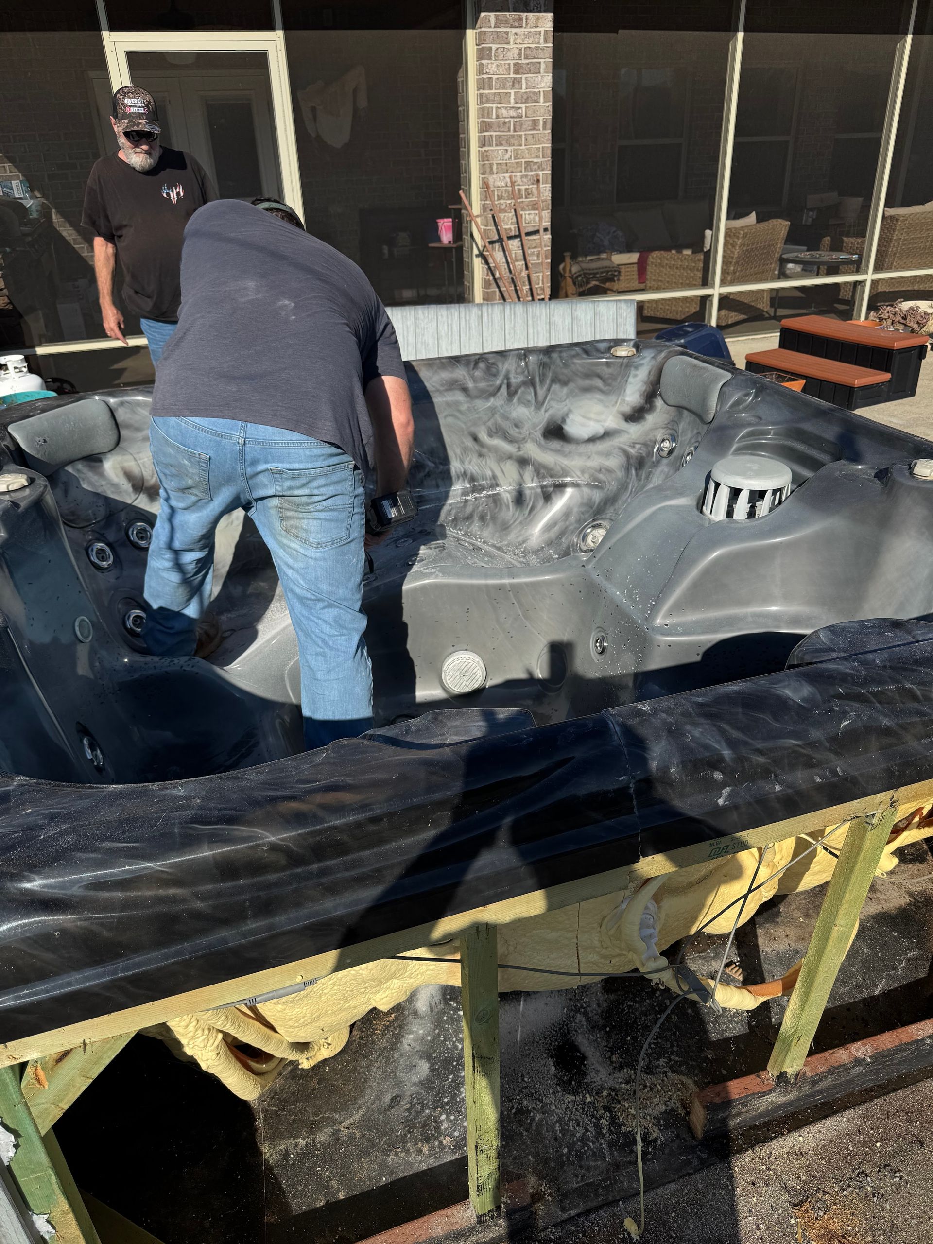 Two people work on a large gray molded panel on a tarp in front of a building.