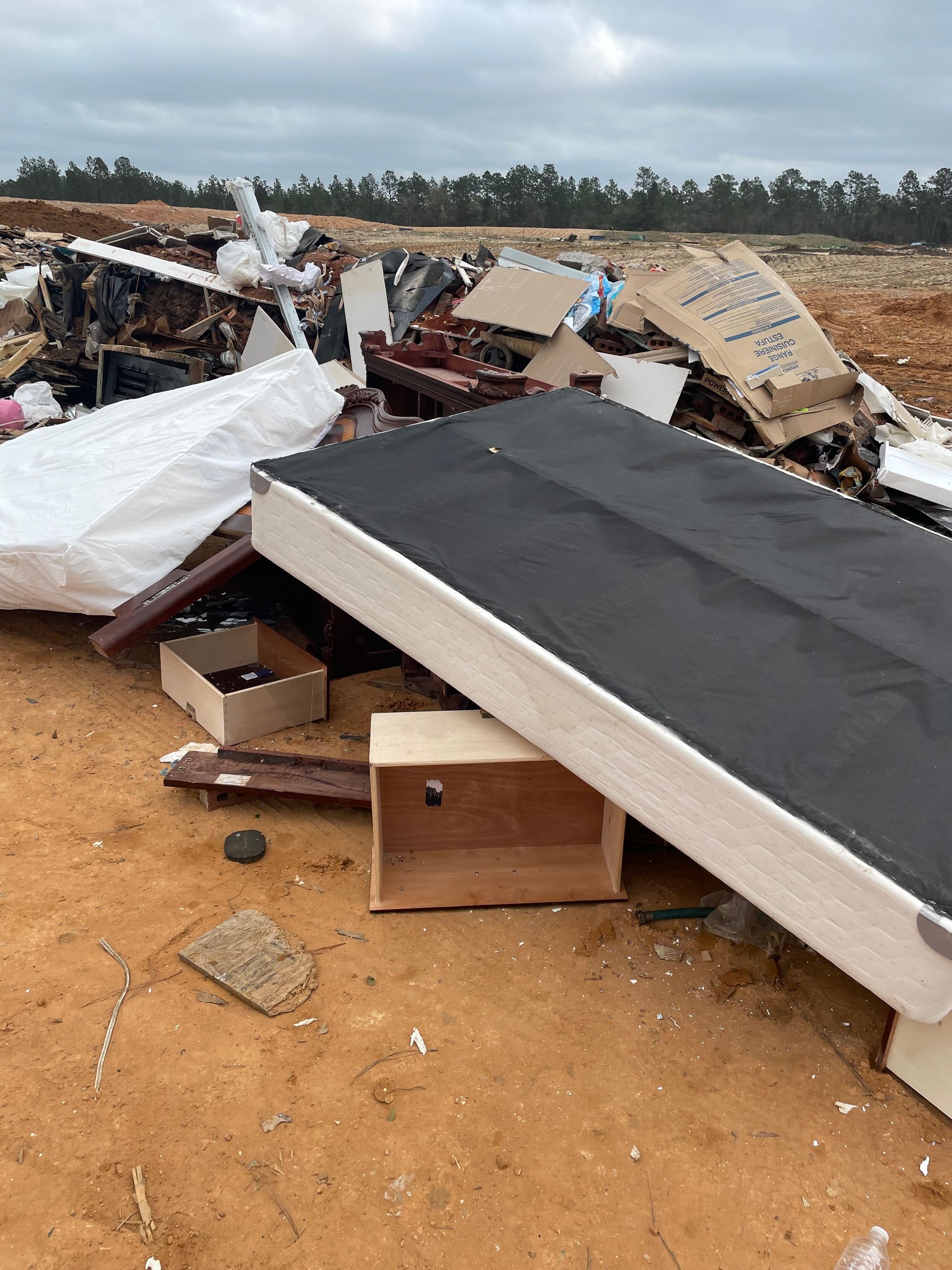 Collapsed building debris scattered on sandy ground, with broken roofing and walls in a rural area.