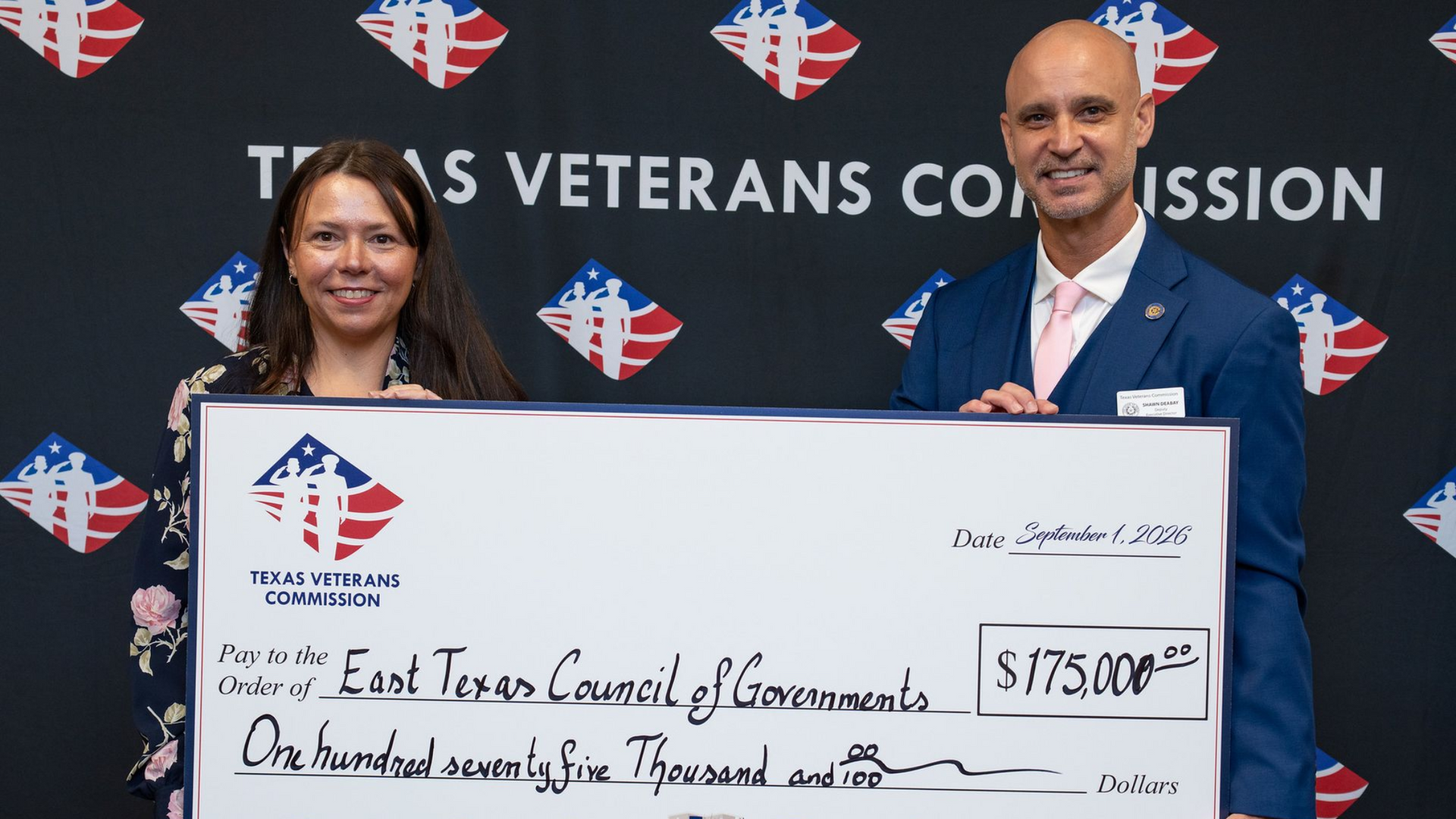 Two people holding a large ceremonial check in front of a Texas Veterans Commission backdrop