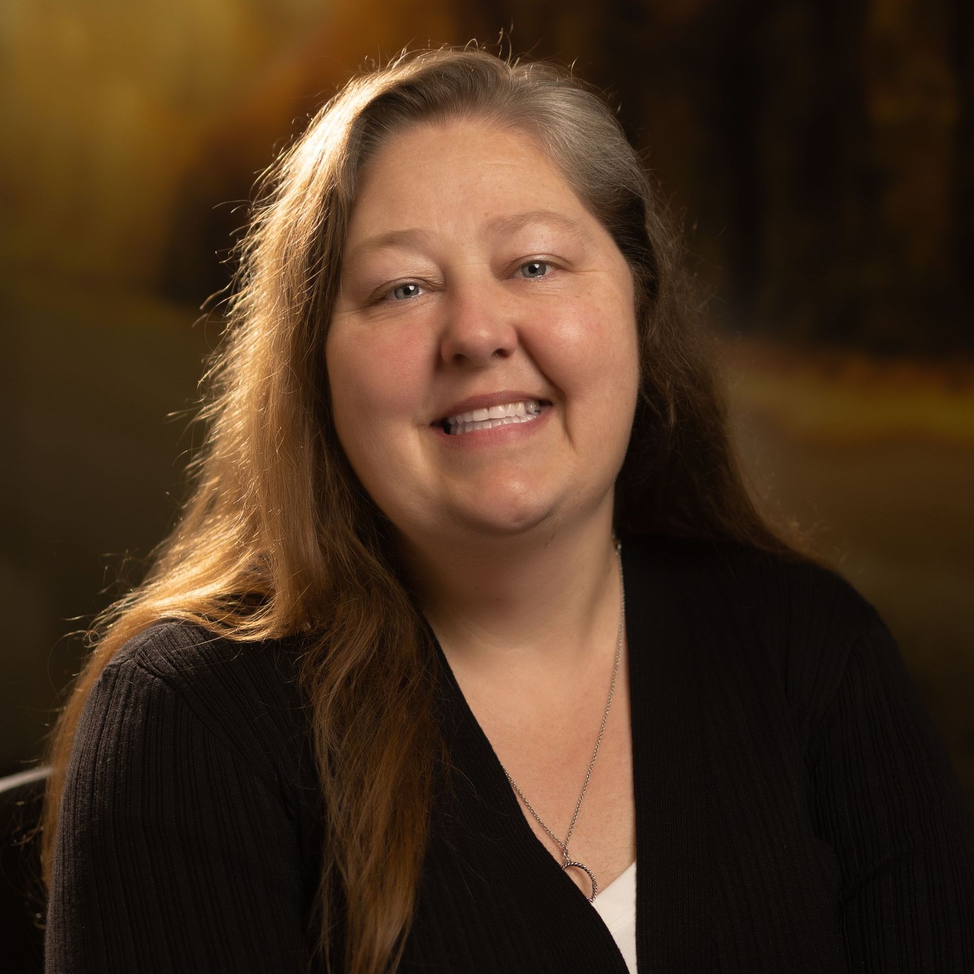A woman wearing a black sweater and a white shirt is smiling for the camera.