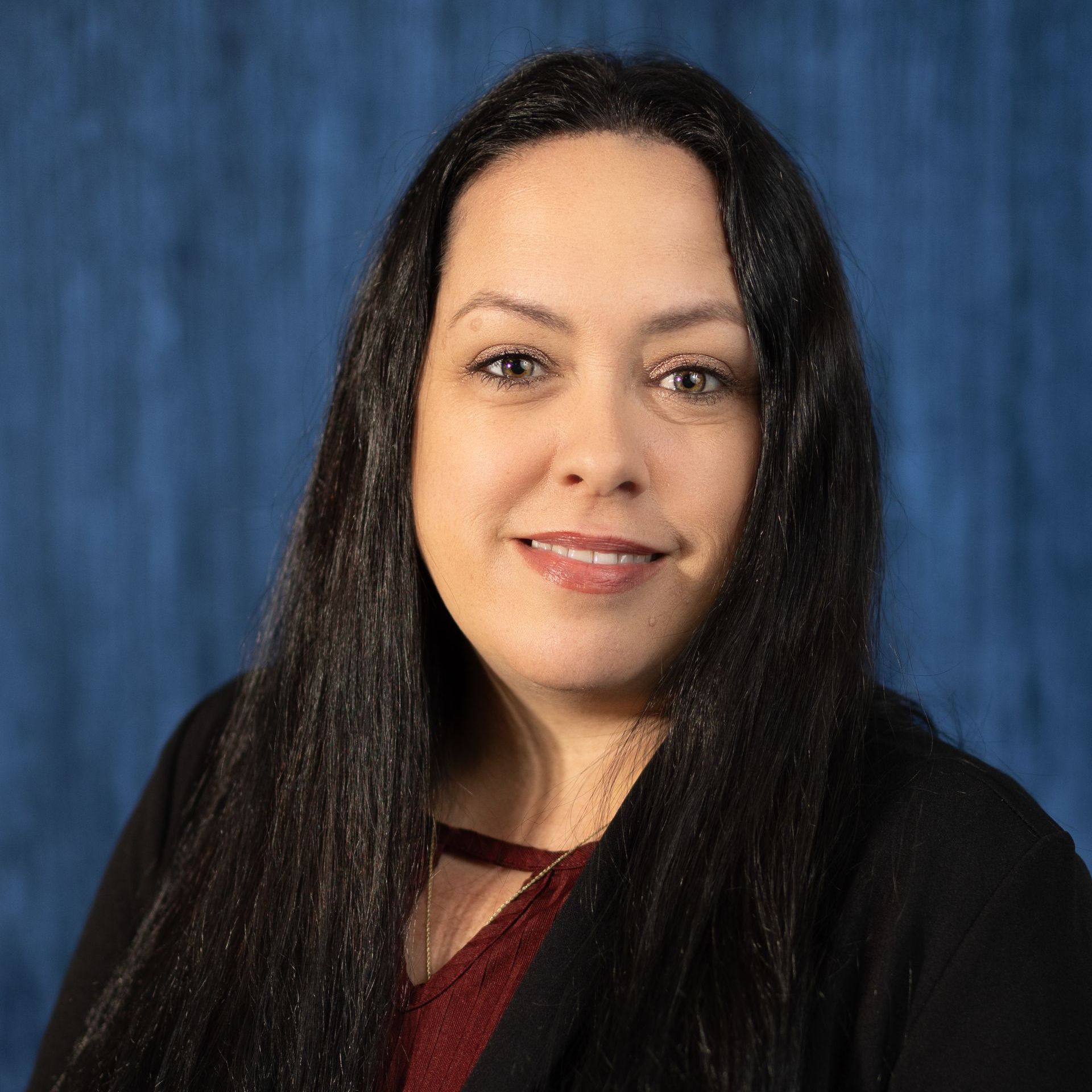 A woman with long black hair is smiling for the camera in front of a blue background.