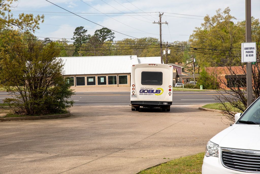 White bus with “GoBus” on back, parked in front of a building with a sign on a sunny day.