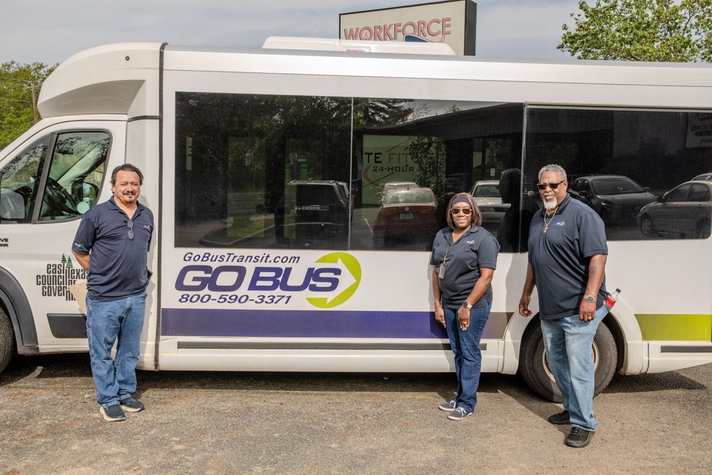 Three people are standing in front of a bus that says go bus