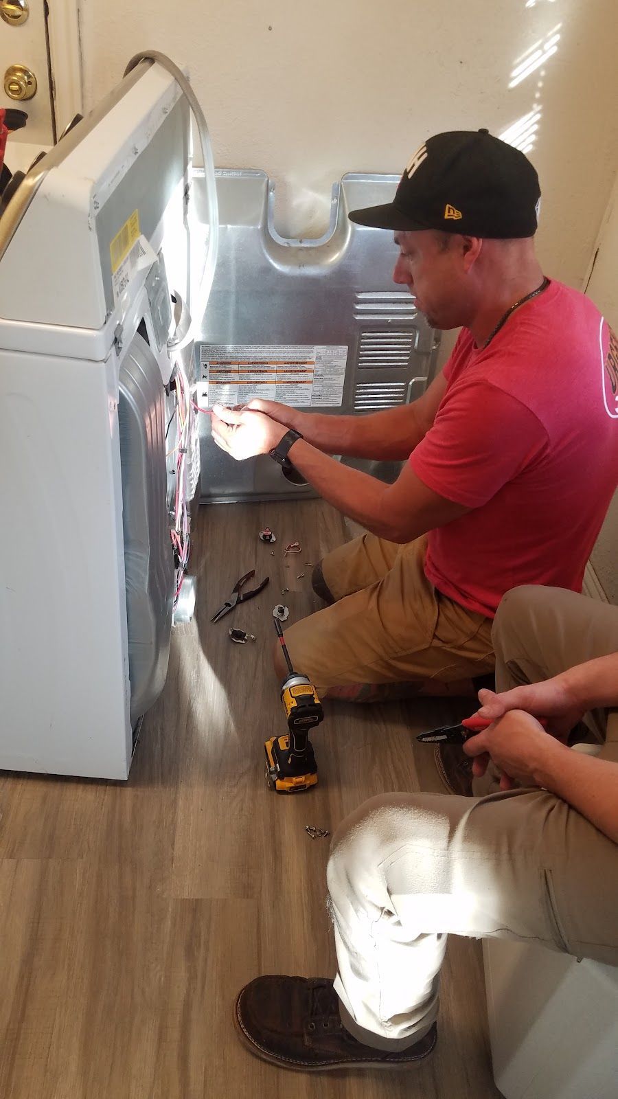 Two men are working on a washing machine in a laundry room.