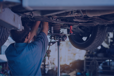 Mechanic working under a car, using tools. The car is on a lift in a garage. | Driver's Choice