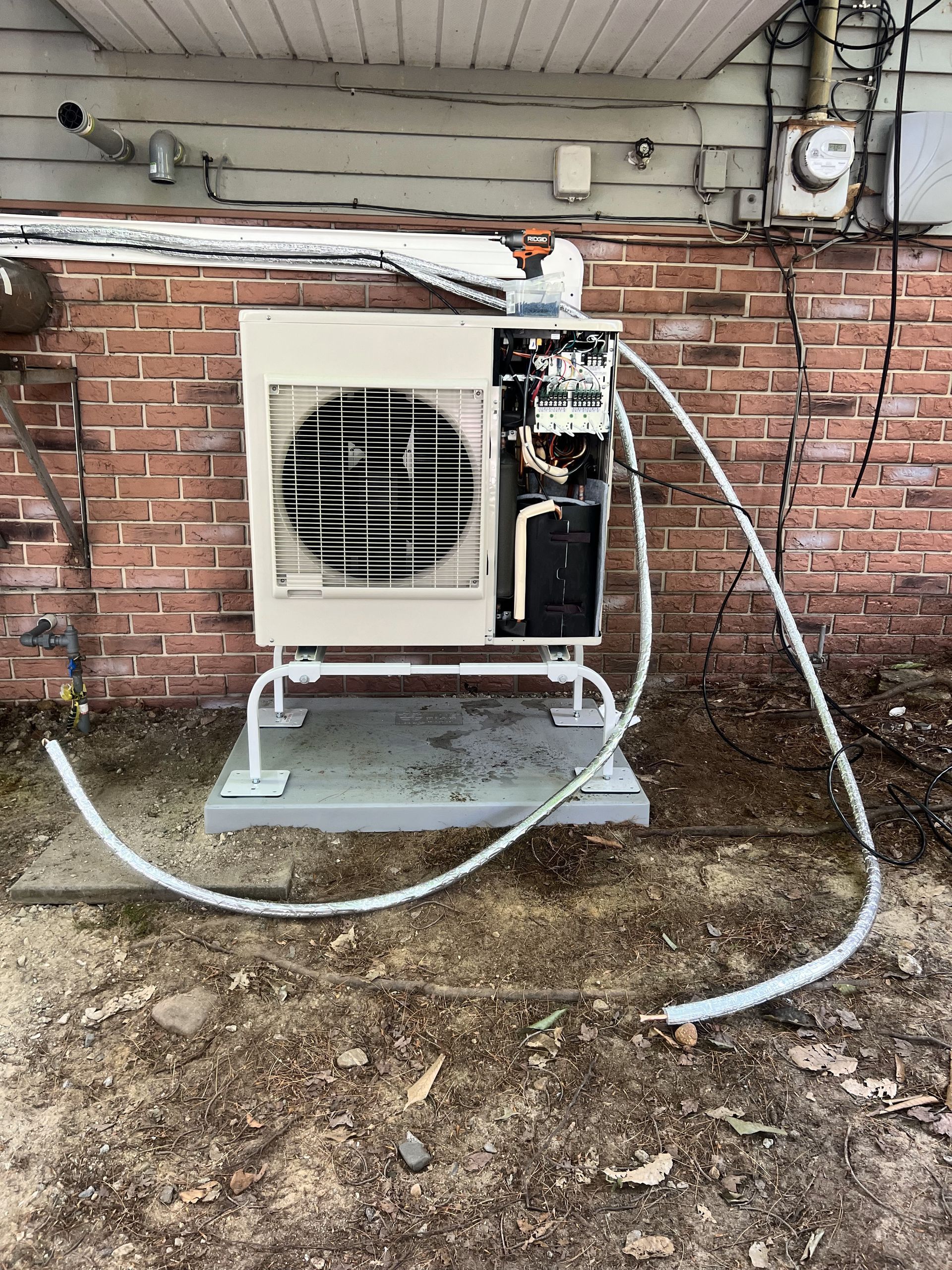 A broken air conditioner is sitting on the ground next to a brick wall.