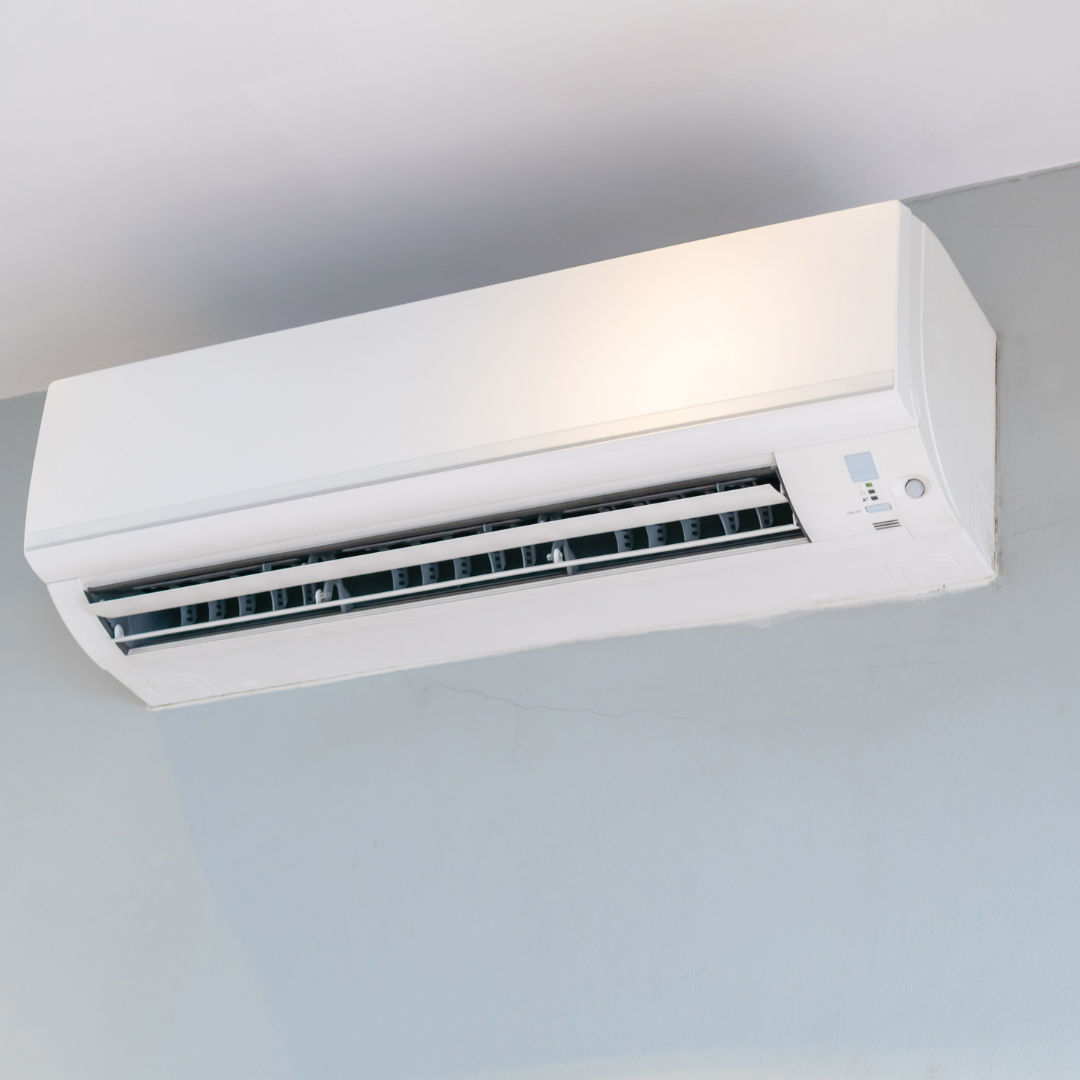 A white air conditioner is mounted to the ceiling in a room.