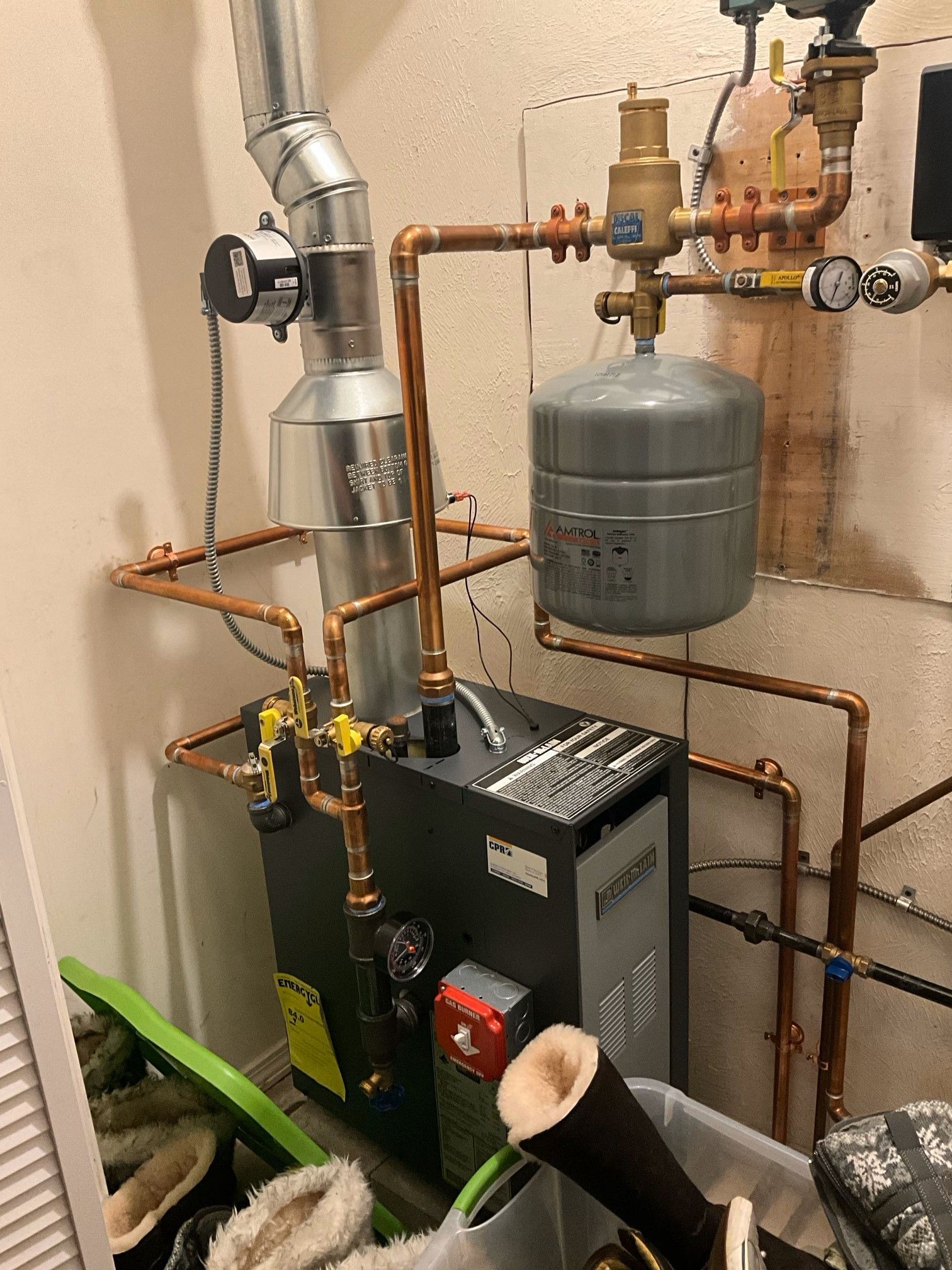 A water heater is sitting in a room surrounded by pipes.