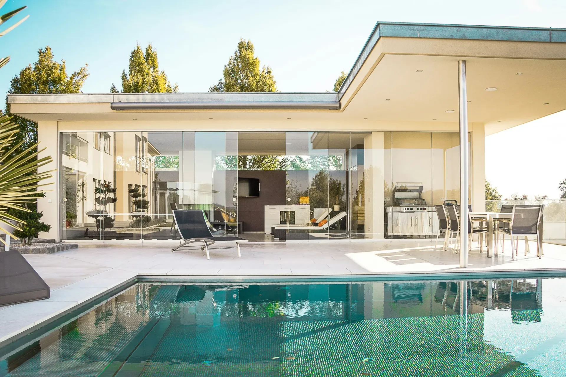 Modern patio with glass walls overlooking a turquoise swimming pool under bright sunlight