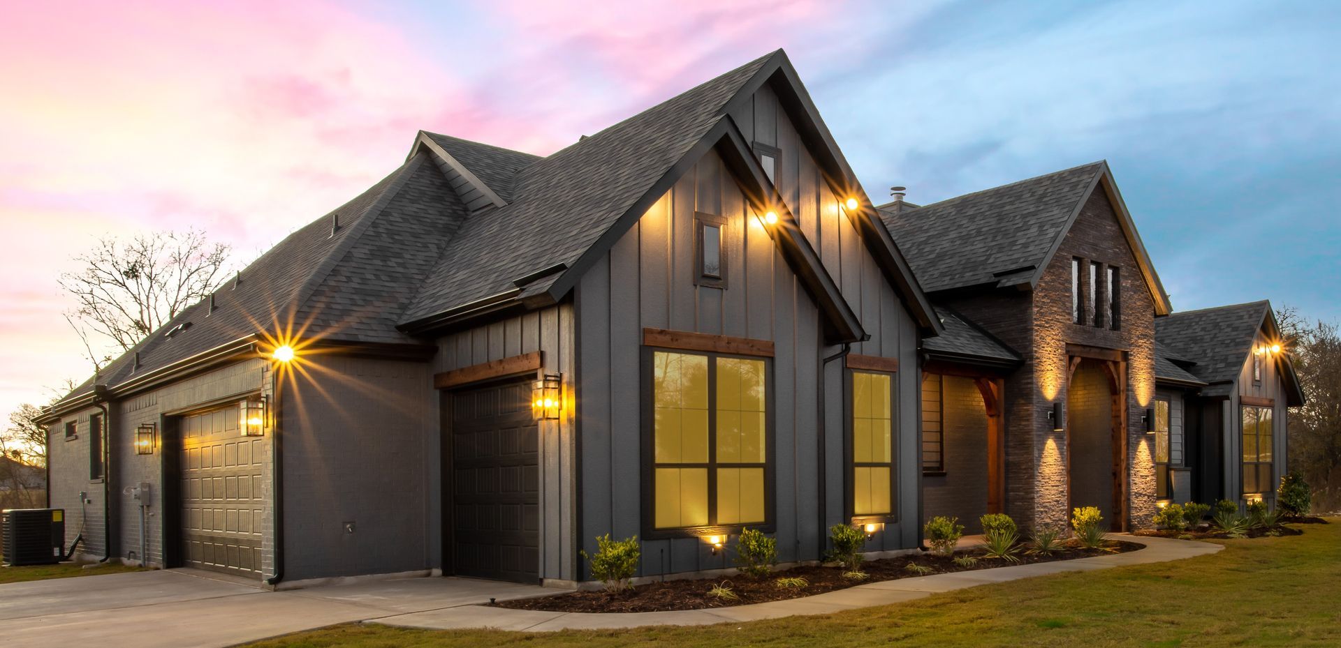 Modern dark-gray suburban house with warm exterior lights at dusk