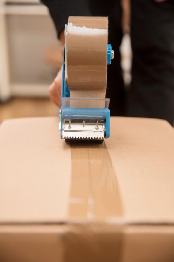 A Person Is Using a Tape Dispenser to Tape a Box — Dunford Removals in Biggenden, QLD