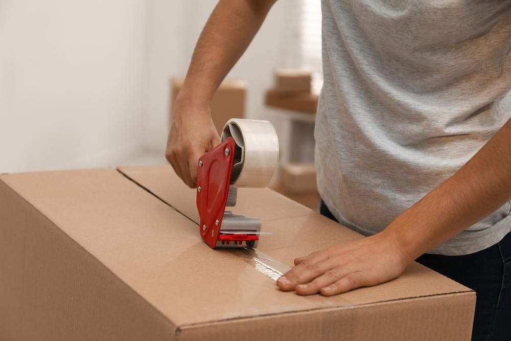 A Person Is Taping a Cardboard Box with Tape — Dunford Removals in Qunaba, QLD