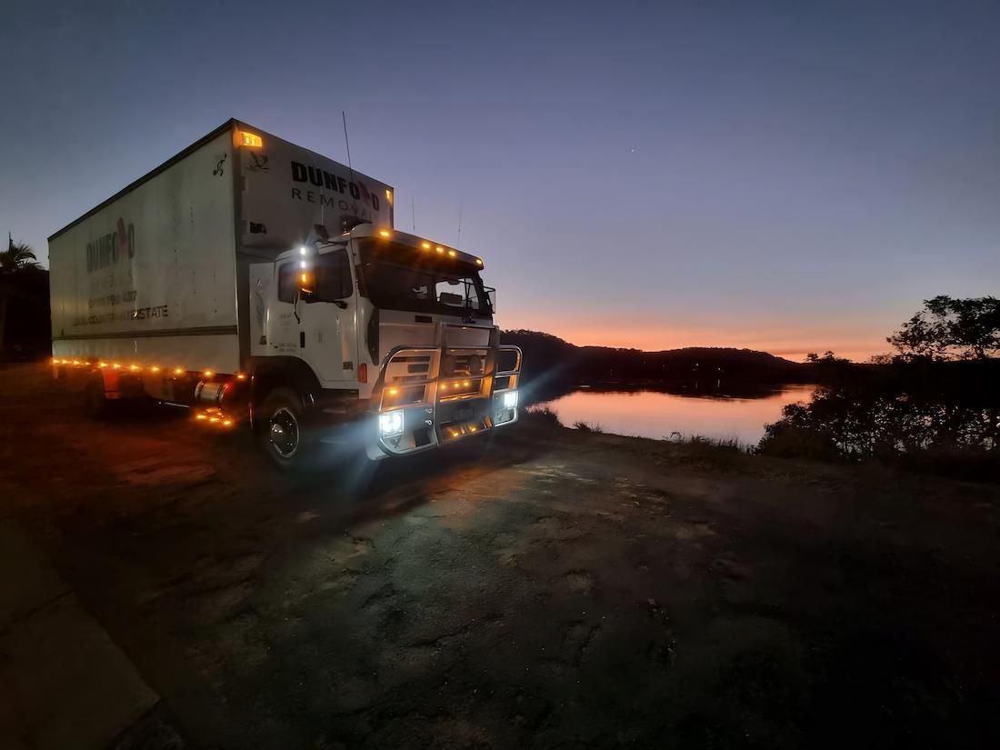 A White Truck is Parked Next to a Body of Water at Night — Dunford Removals in Qunaba, QLD