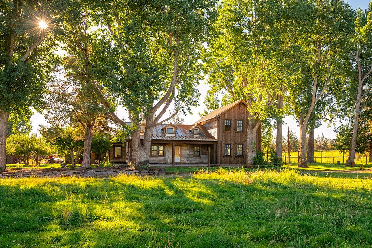A house is sitting in the middle of a grassy field surrounded by trees.