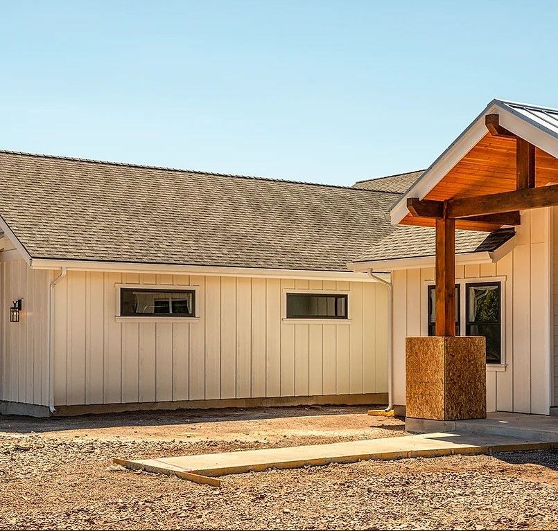 A white house with a porch and a metal roof is sitting on top of a dirt field