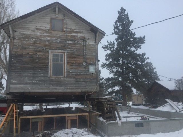 An old wooden house is being raised on stilts in the snow.