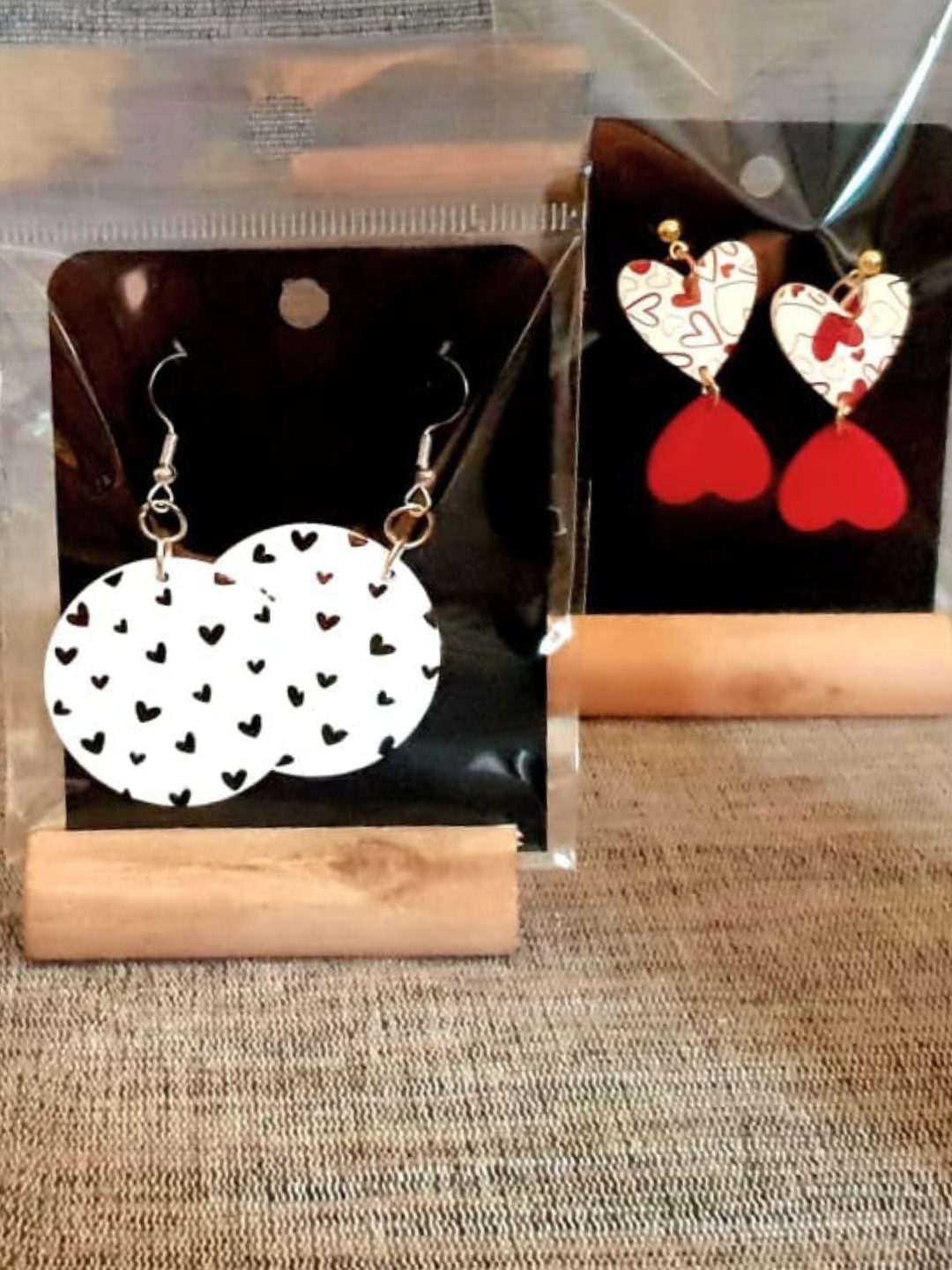 Boucles d'oreilles pendantes rouges et blanches en forme de cœur présentées sur des supports transparents.