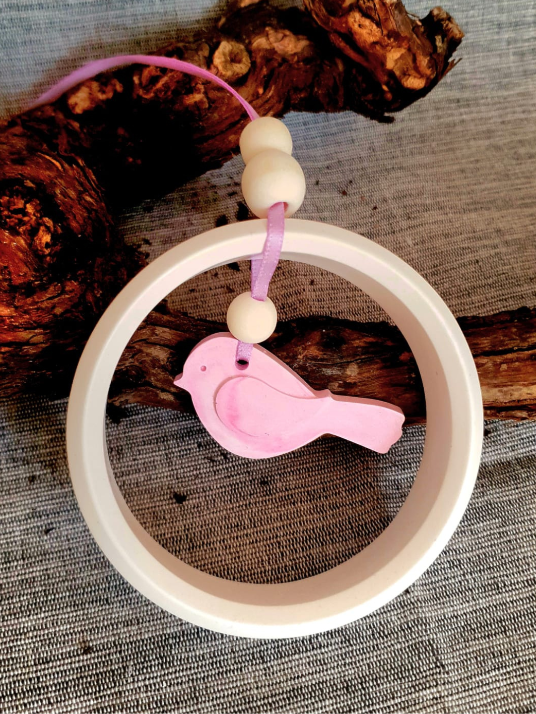 Breloque oiseau rose suspendue à l'intérieur d'un anneau blanc sur un fond de tissu texturé