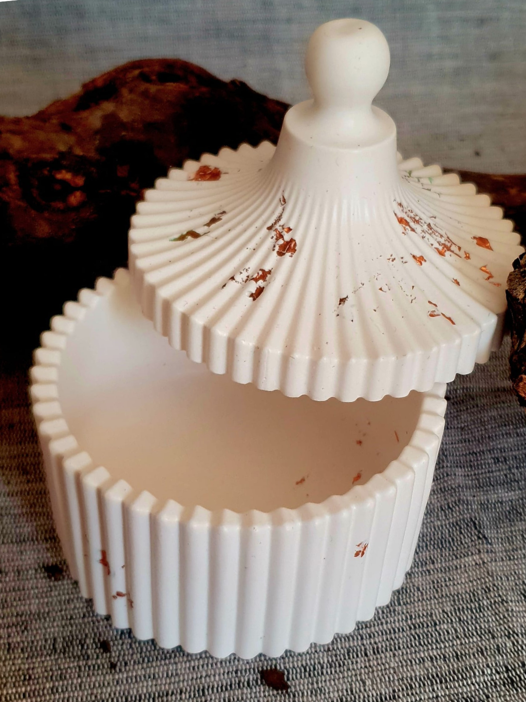 Boîte décorative blanche côtelée avec couvercle et poignée à bouton, légèrement ouverte, sur une surface texturée