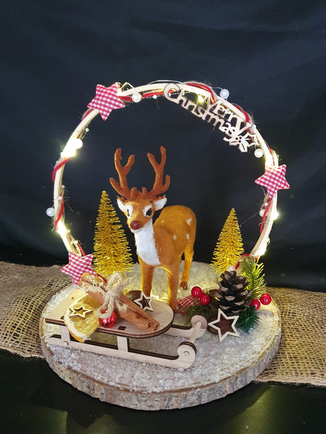 Figurine de cerf de Noël sur un socle rond avec des lumières, des sapins et un nœud rouge sur fond sombre