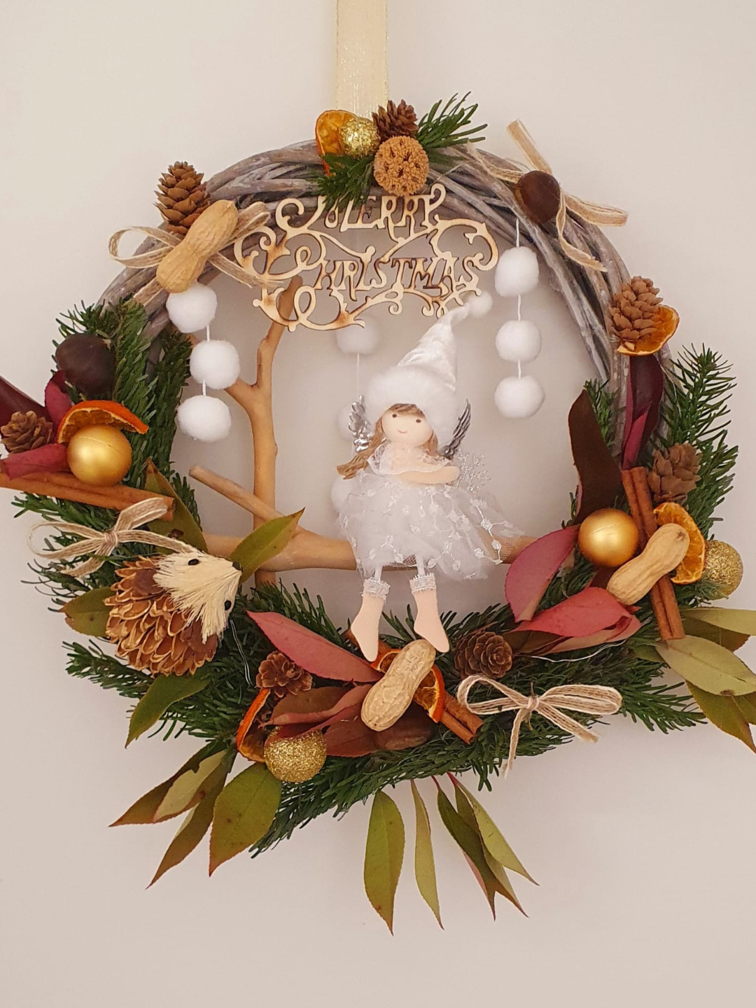 Couronne florale décorative avec une petite figurine d'ange et des baies blanches sur fond neutre