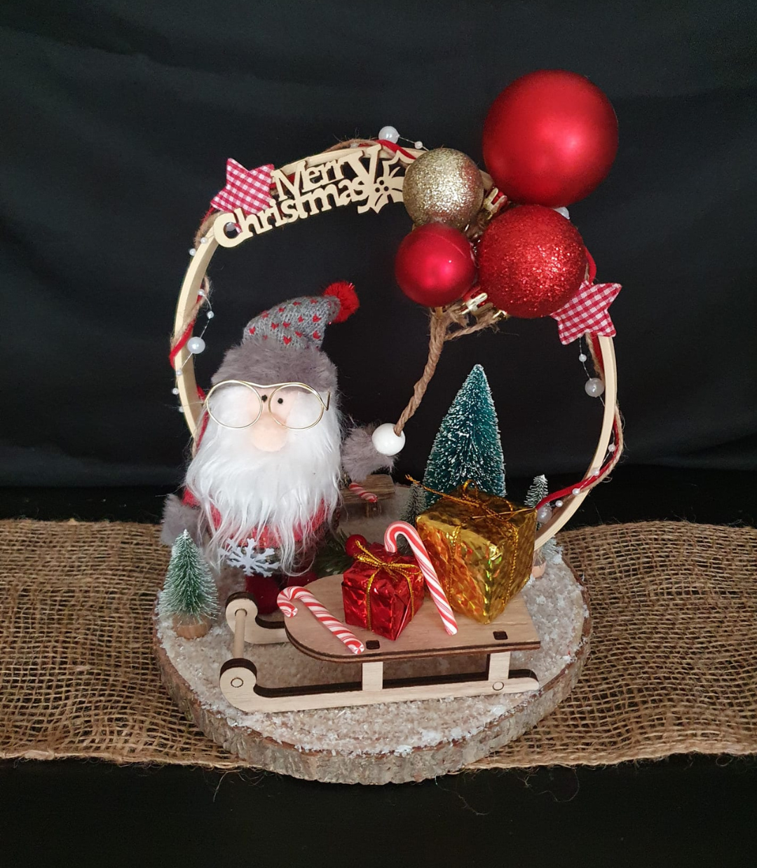 Figurine du Père Noël avec décorations de Noël, ornements rouges et boîtes cadeaux sur un socle rond