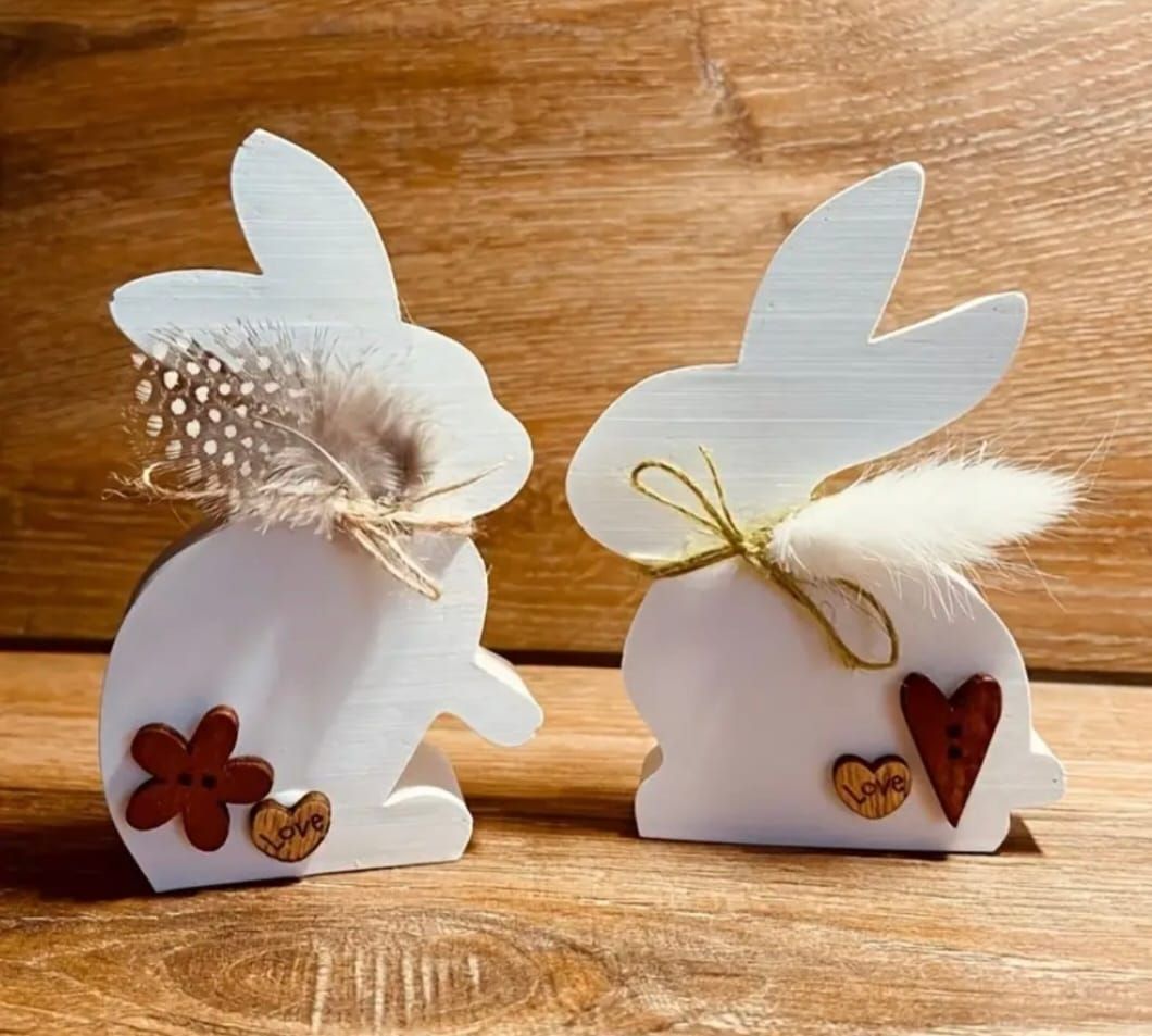 Deux décorations de Pâques blanches en forme de lapin, avec des fleurs et de la ficelle, sur une surface en bois.