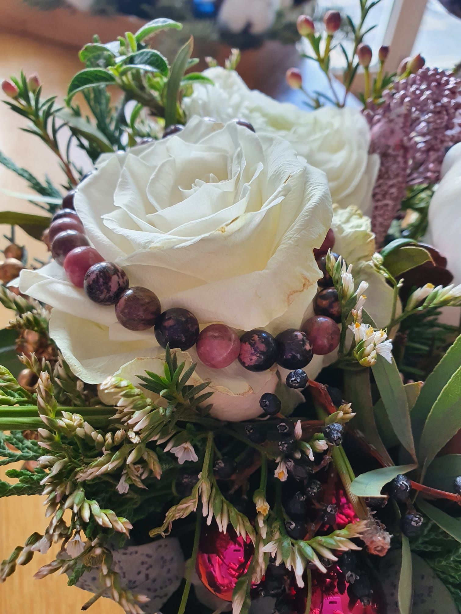 Des roses blanches ornées d'une guirlande de perles foncées, dans une composition florale agrémentée de feuillage vert.