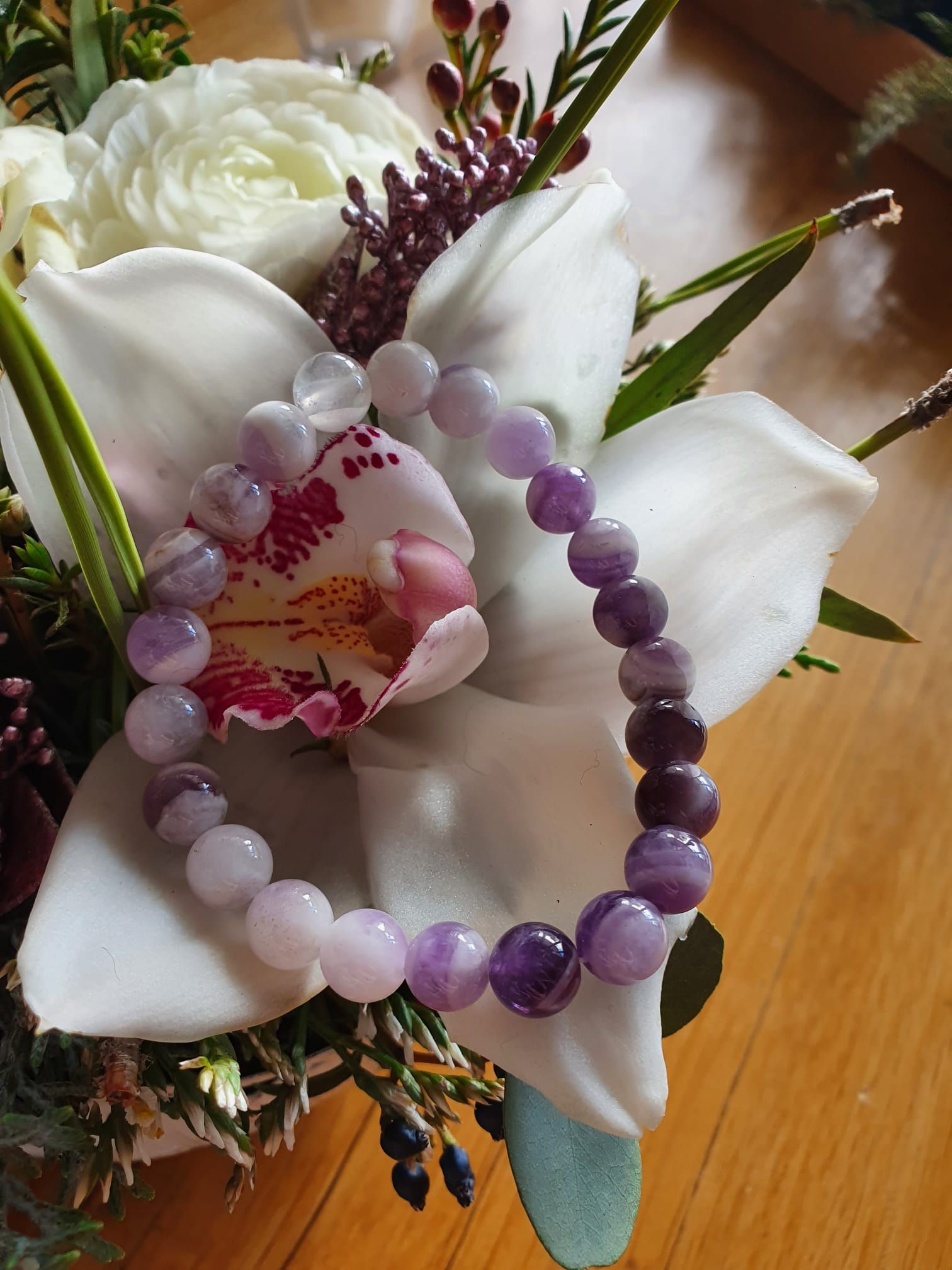 Bracelet de perles violettes posé sur des orchidées et des fleurs blanches