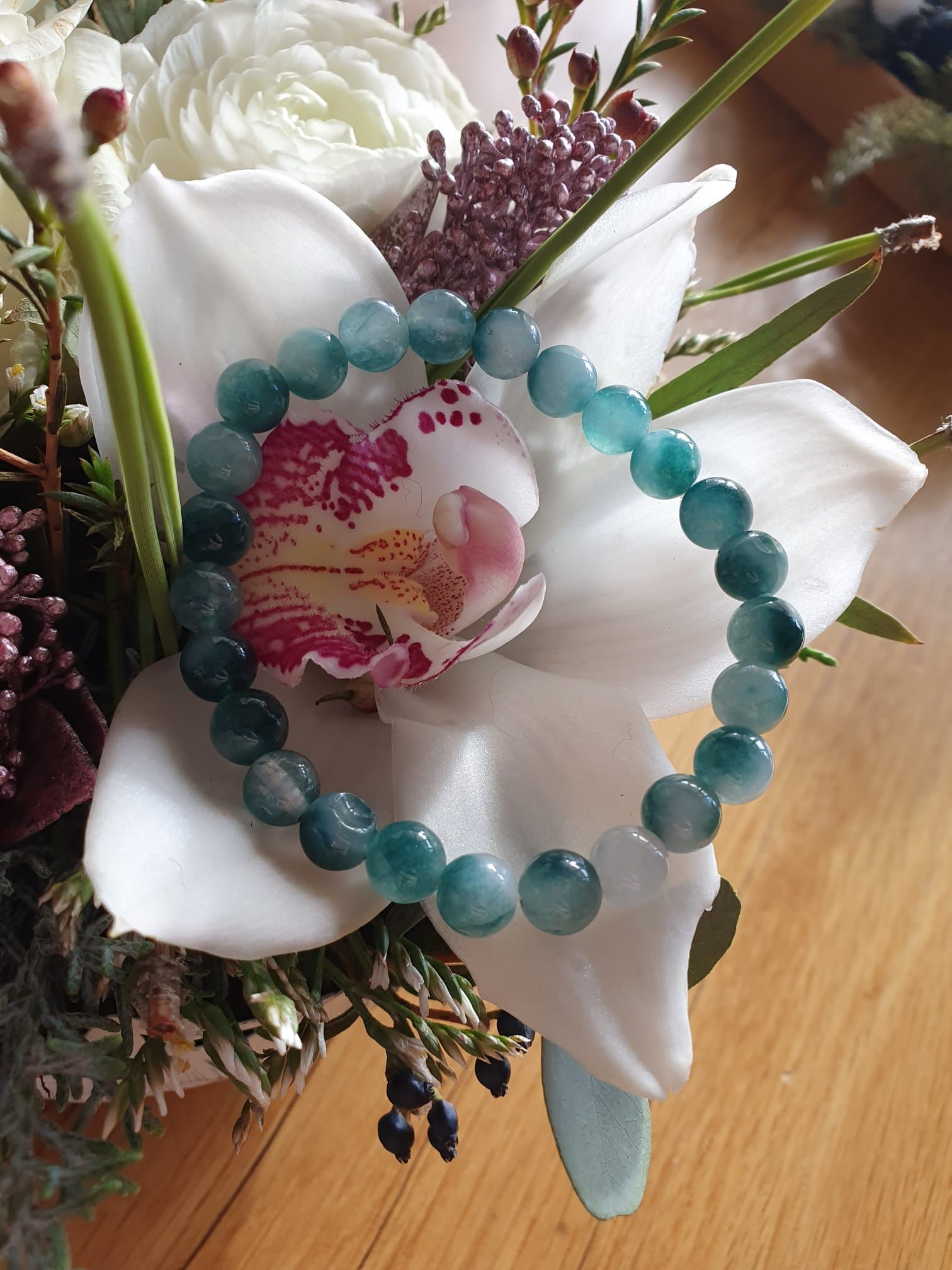 Bracelet de perles turquoise reposant sur des fleurs blanches avec une orchidée rose en son centre
