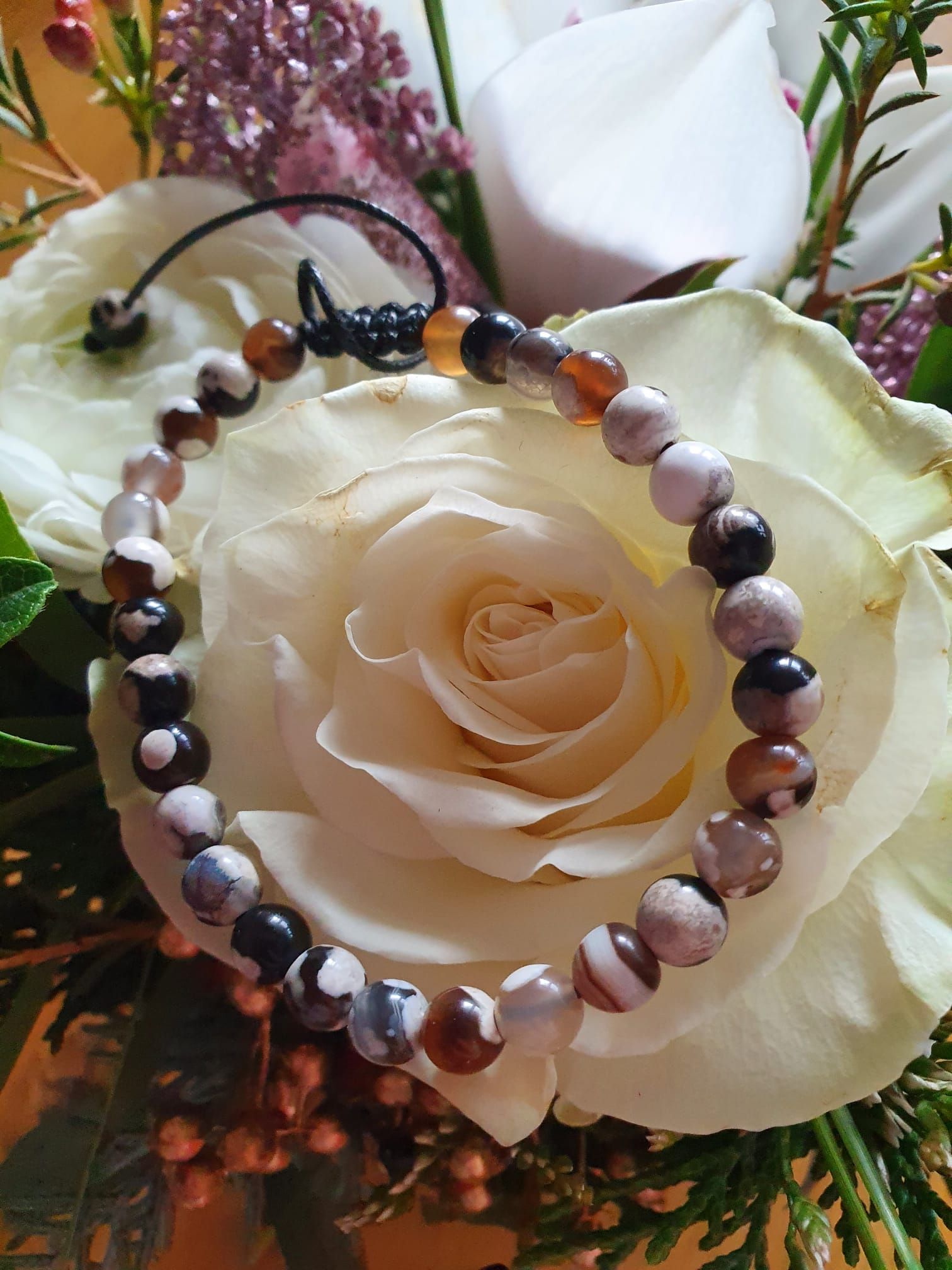Bracelet de perles sur une rose crème avec feuillage et fleurs violettes