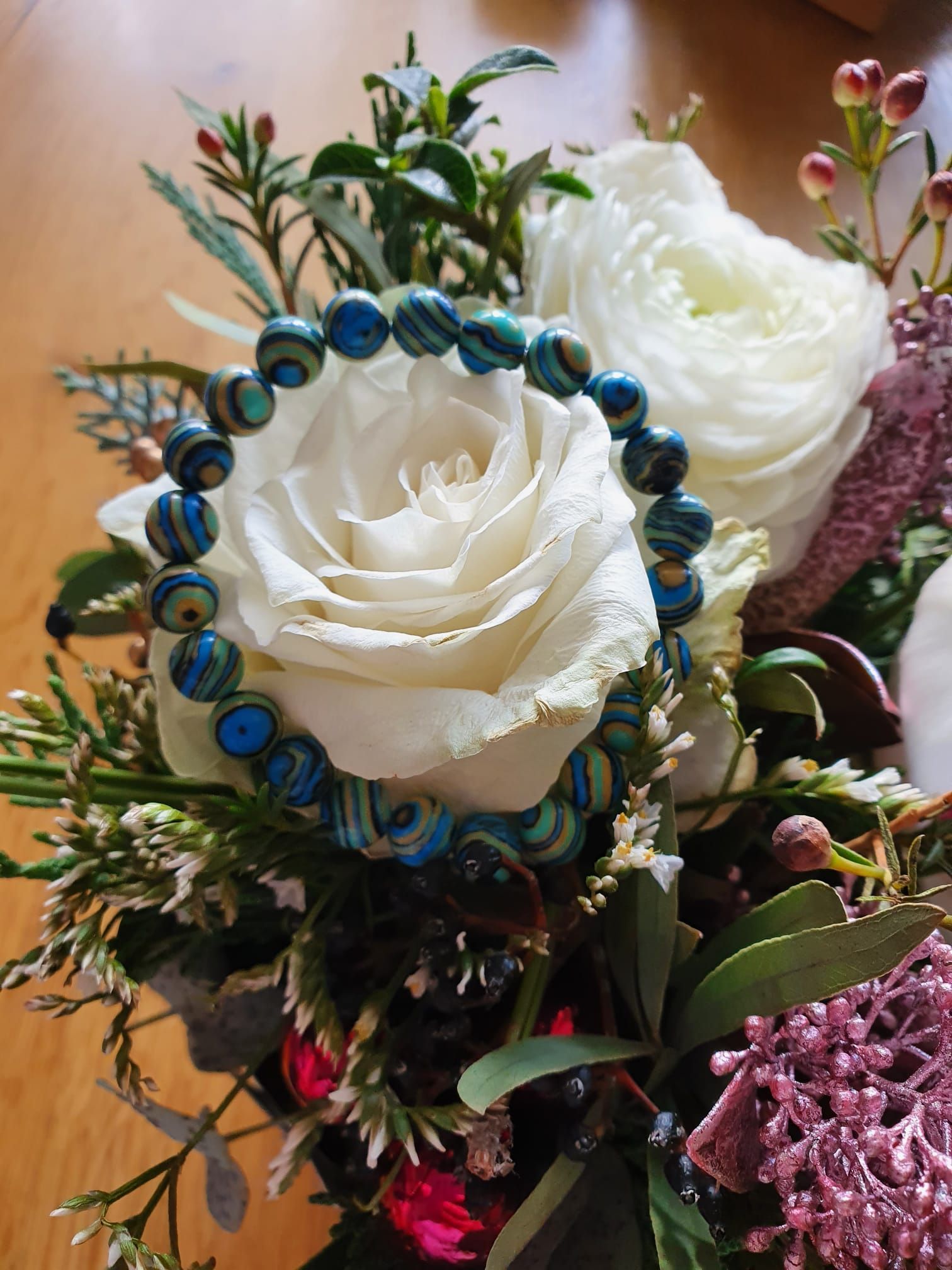 Des roses blanches et un bracelet de perles bleues parmi un arrangement floral rose et vert