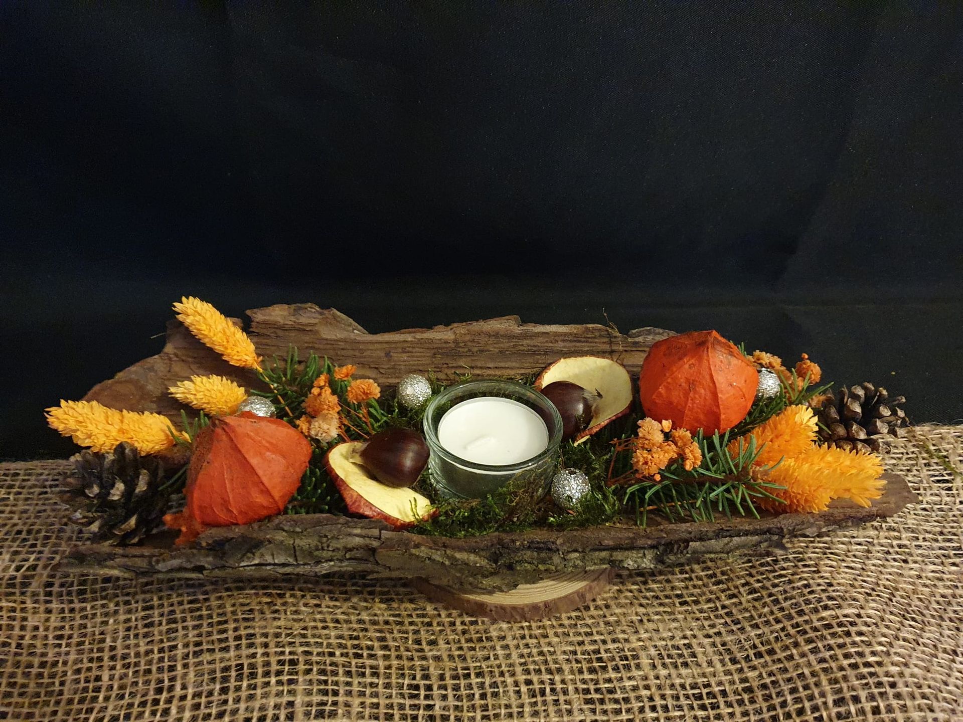 Centre de table automnal composé de citrouilles, de courges, de pommes de pin, de feuilles et d'une bougie blanche.