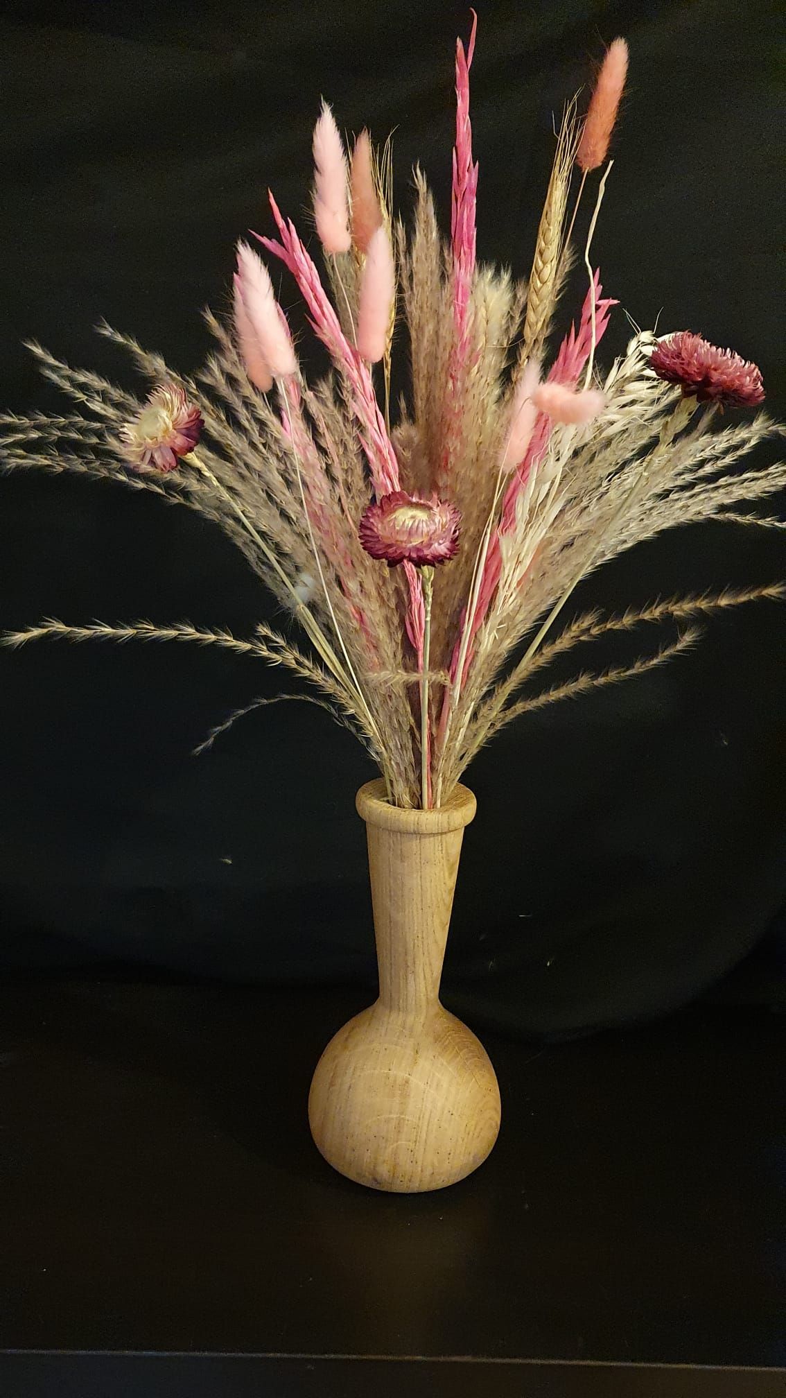 Herbes décoratives séchées et fleurs roses dans un vase beige sur fond noir