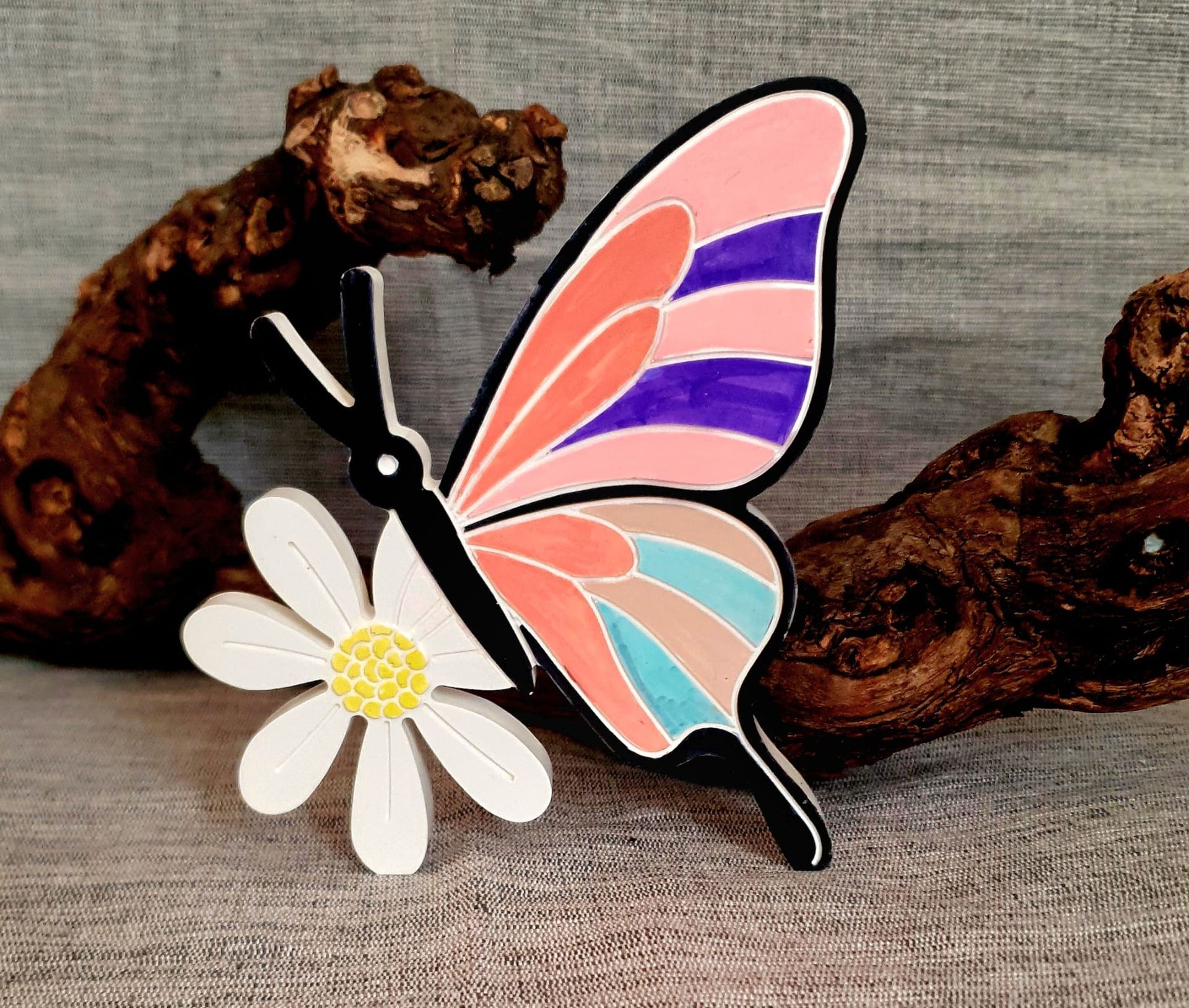 Broche décorative papillon noir aux ailes pastel et marguerite blanche sur fond de tissu gris