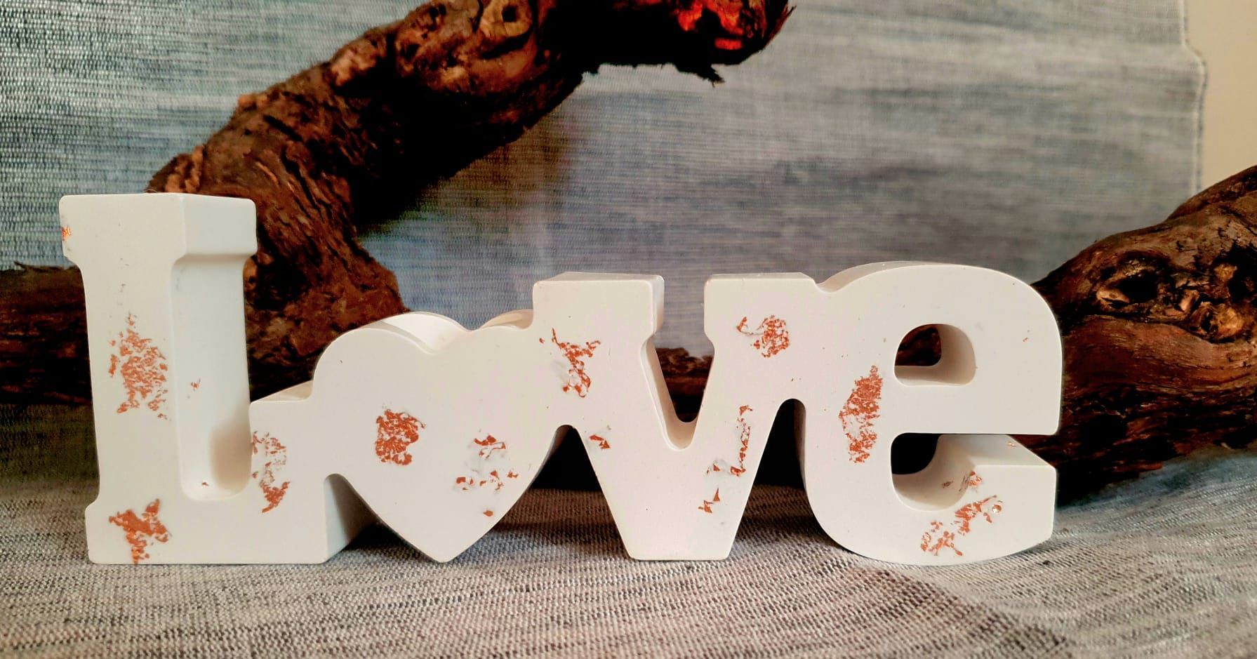 Panneau blanc « Love » orné de motifs floraux sur une surface rustique, avec des branches en arrière-plan.
