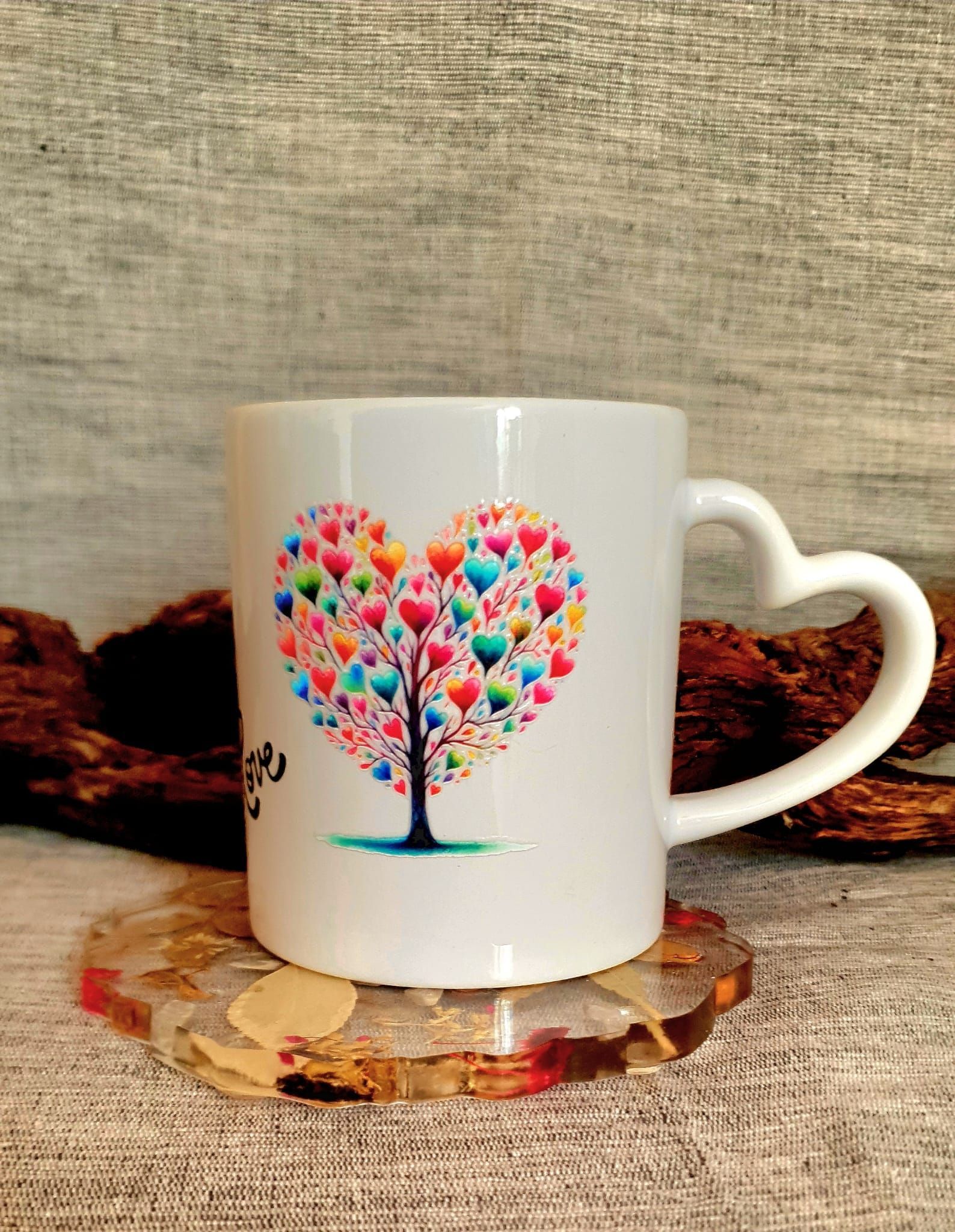 Mug blanc orné d'un motif d'arbre coloré en forme de cœur et d'une anse en forme de cœur sur un fond texturé.