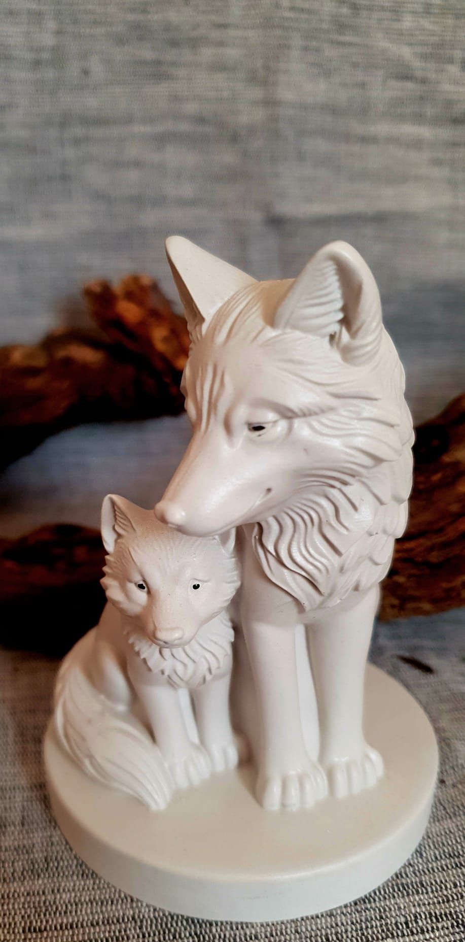 Figurine en céramique blanche représentant un renard et son petit, sur un socle rond.