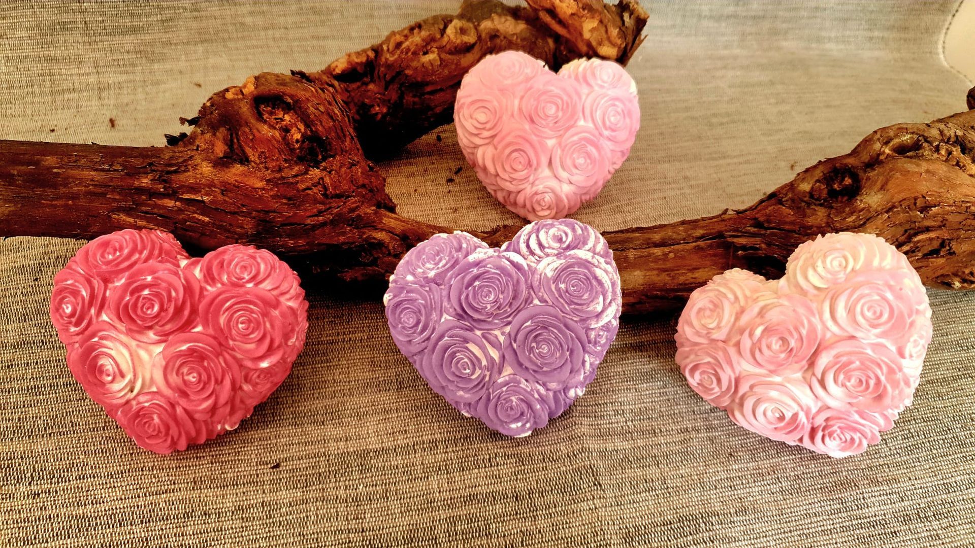 Quatre savons décoratifs en forme de cœur, roses et lavande, disposés sur de la toile de jute avec du bois flotté.