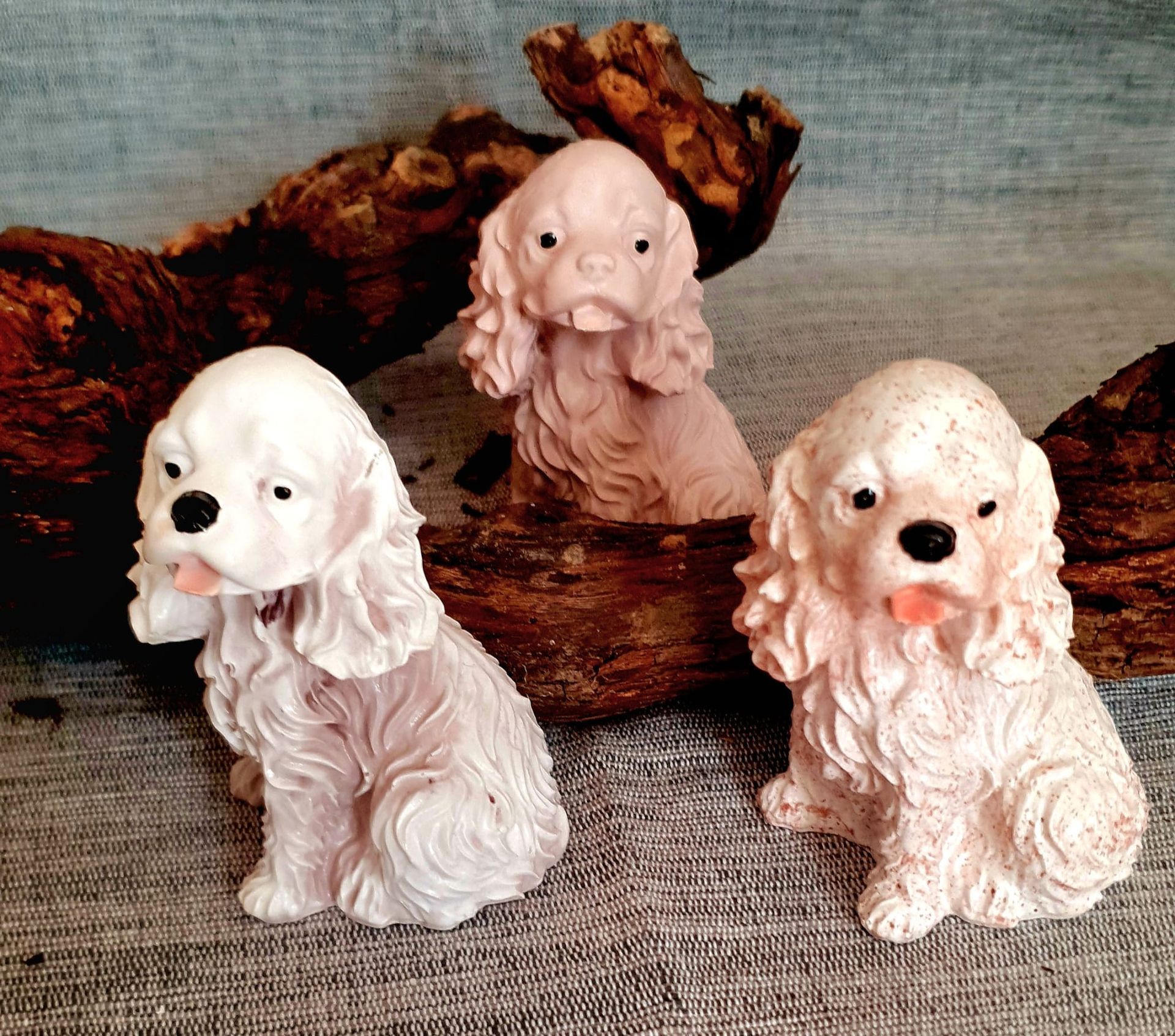 Trois petites figurines de spaniels en porcelaine sur un fond de tissu rustique, deux blanches au premier plan.