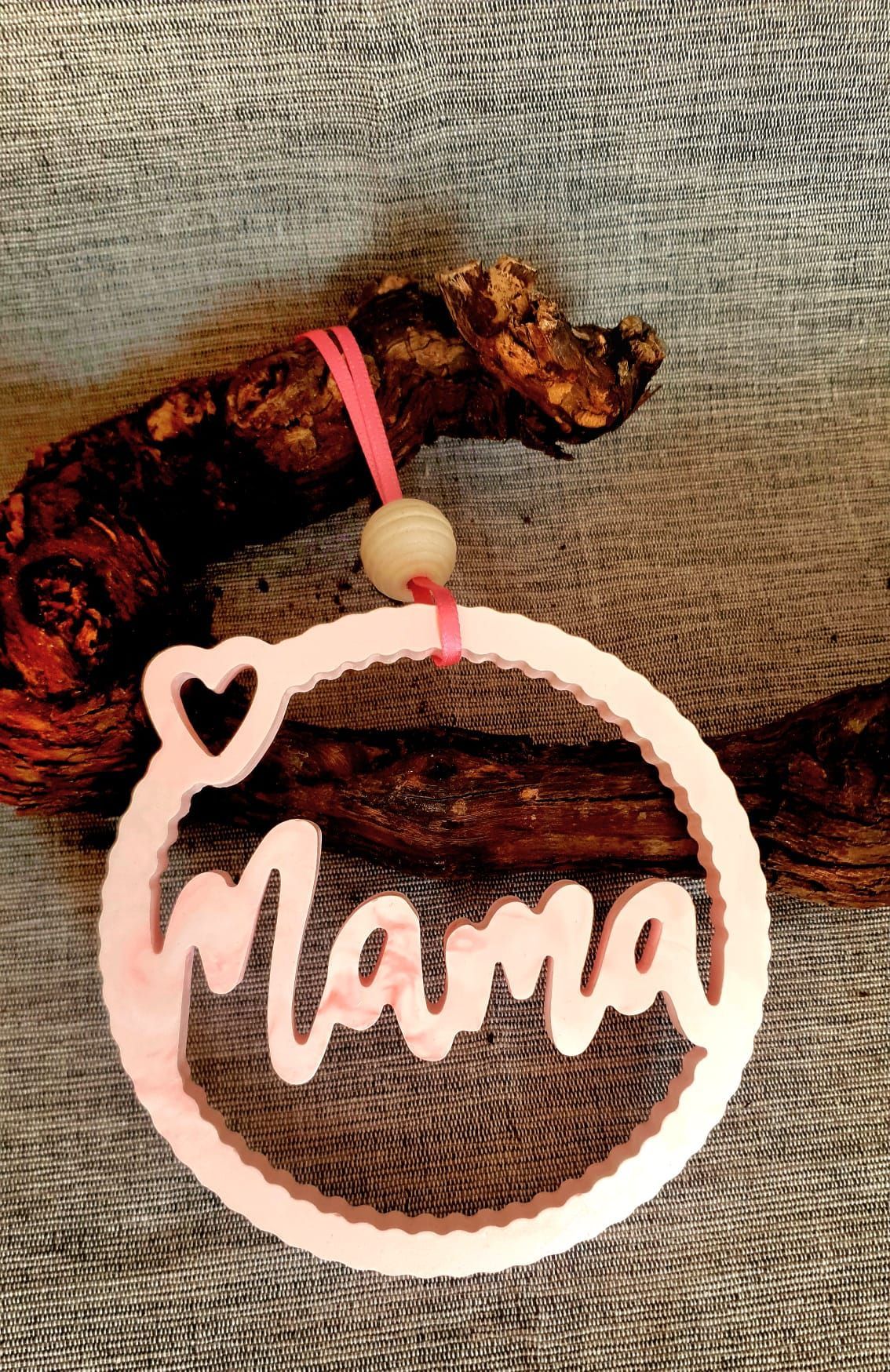 Ornement rose « Maman » suspendu à côté d'une figurine de cheval marron sur un fond de tissu gris.