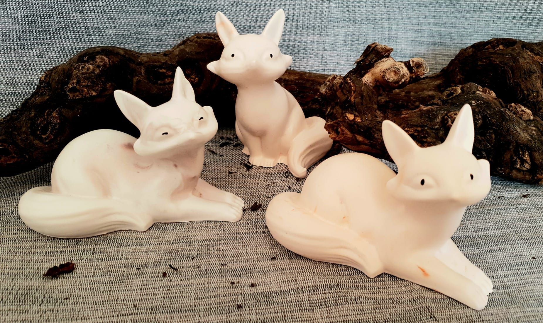 Trois petites figurines de renards blancs sur une surface en tissu texturé avec un fond sombre