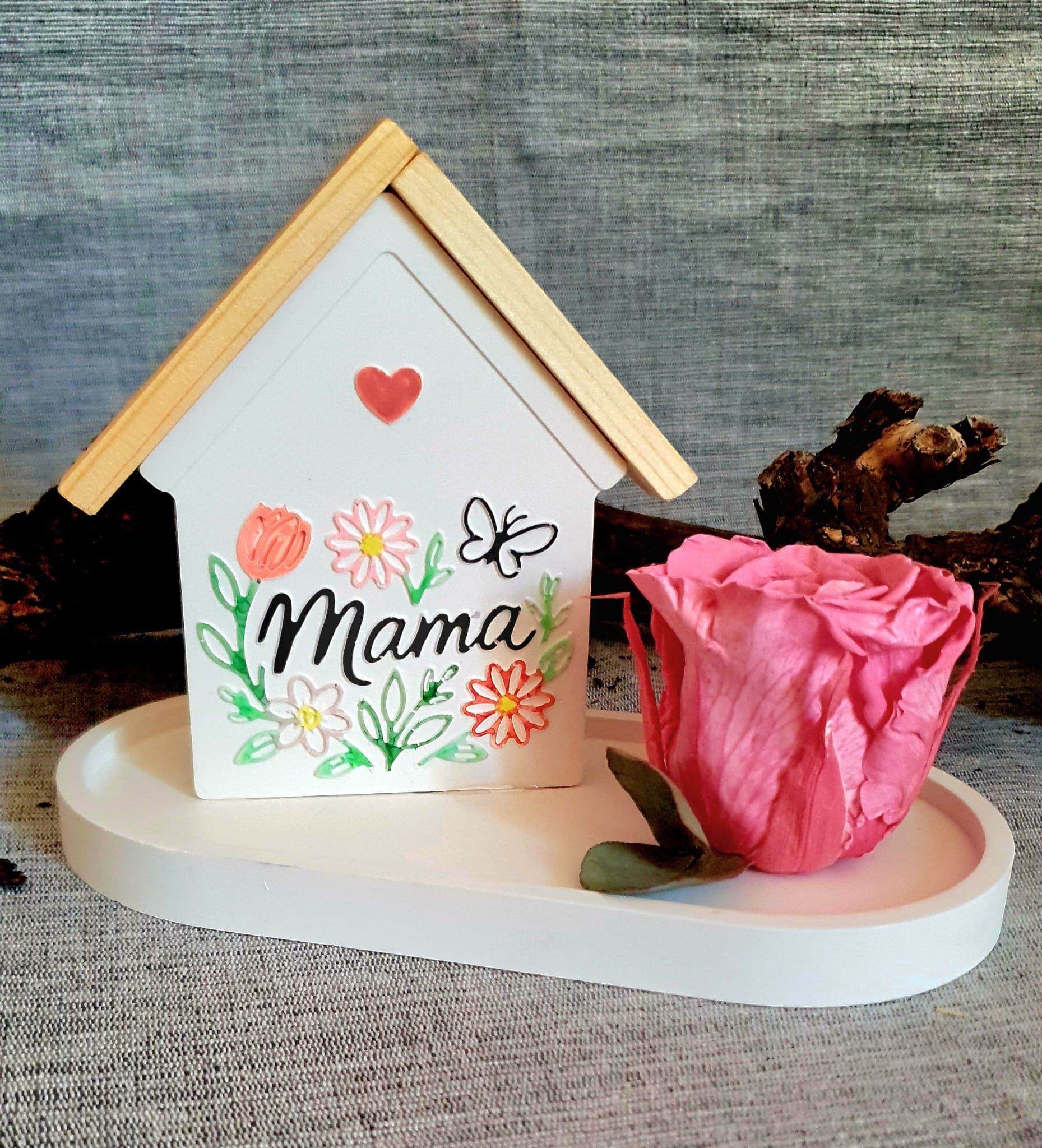 Un bocal Mason décoré du mot « maman » sur un plateau blanc, à côté d'une fleur rose et d'un papillon.
