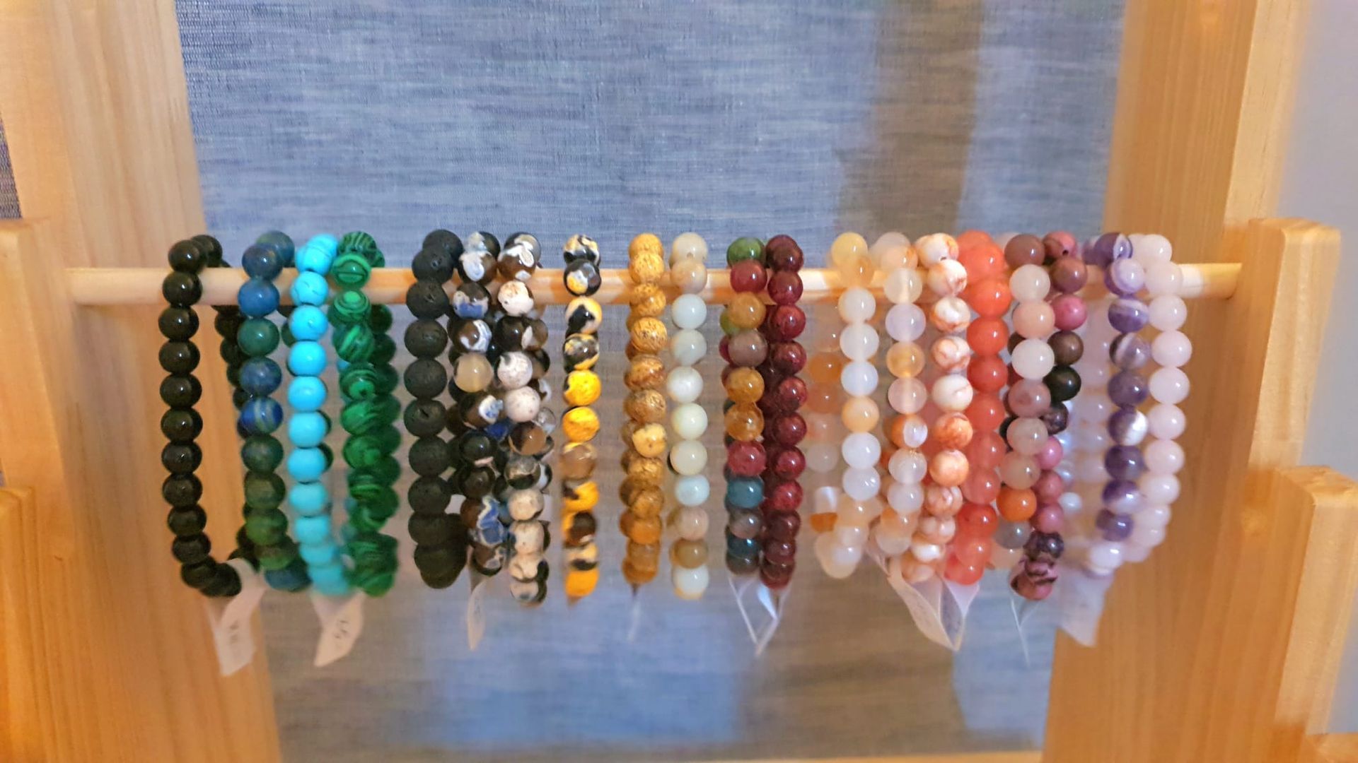 Bracelets de perles colorées disposés en rangées sur un présentoir en bois sur fond gris