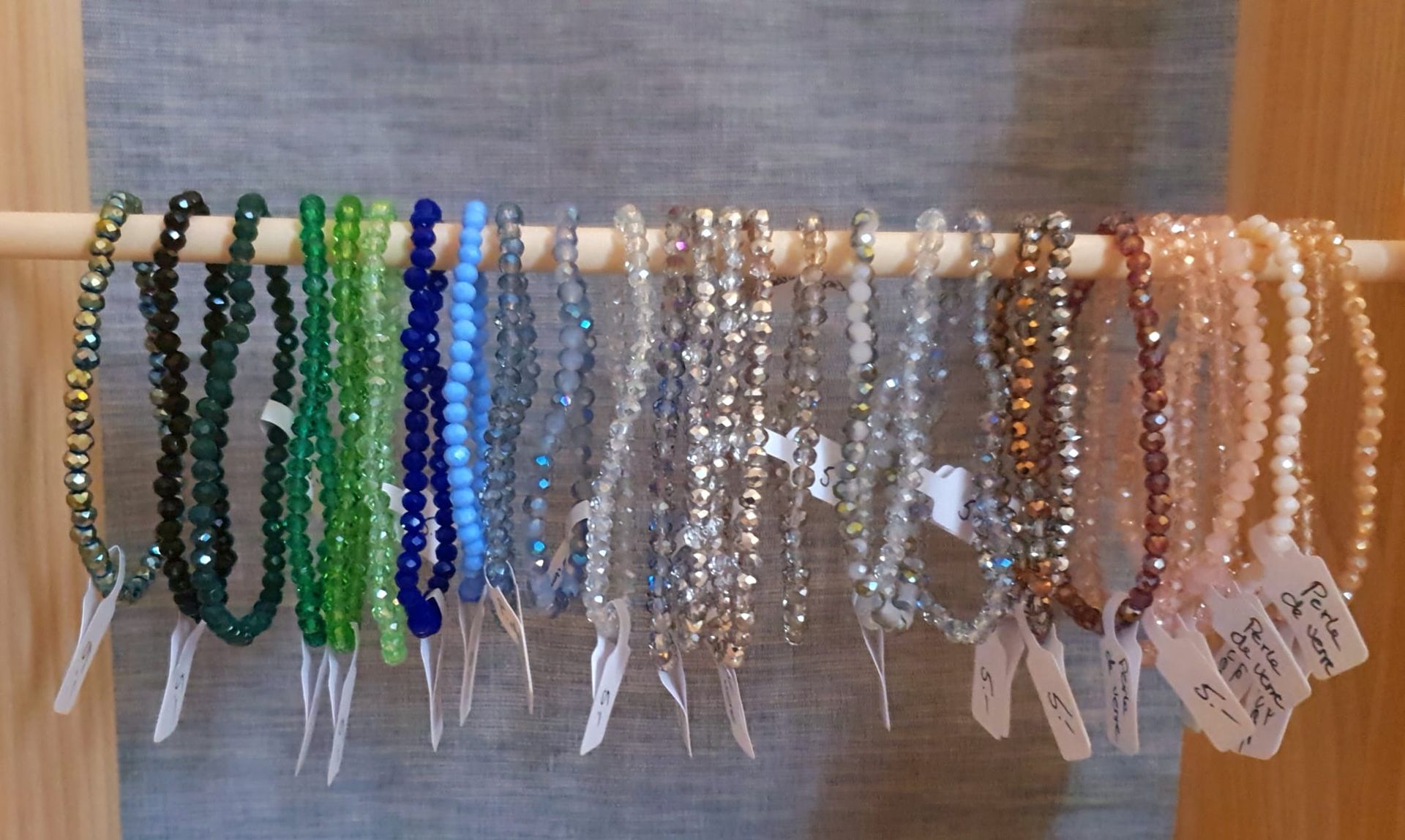 Des rangées de colliers de perles colorées sont suspendues à un présentoir en bois.
