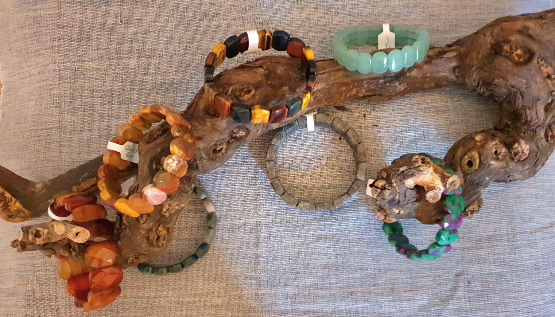 Présentoir en bois avec plusieurs bracelets de perles marron, vertes, turquoise et multicolores.