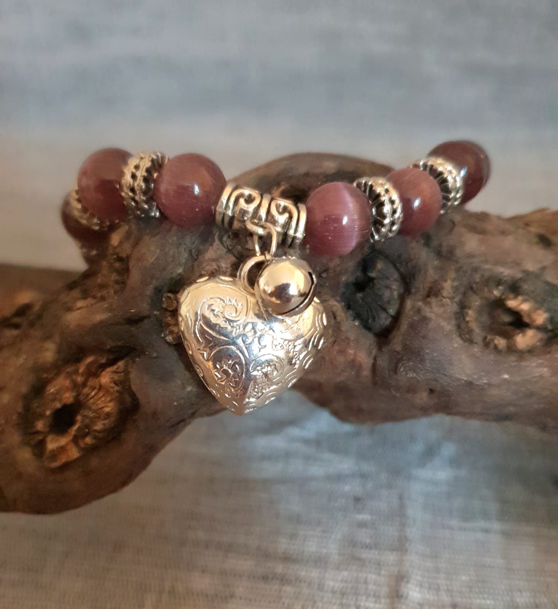 Bracelet à breloques avec un pendentif en forme de cœur argenté et des perles rouges sur une branche rustique