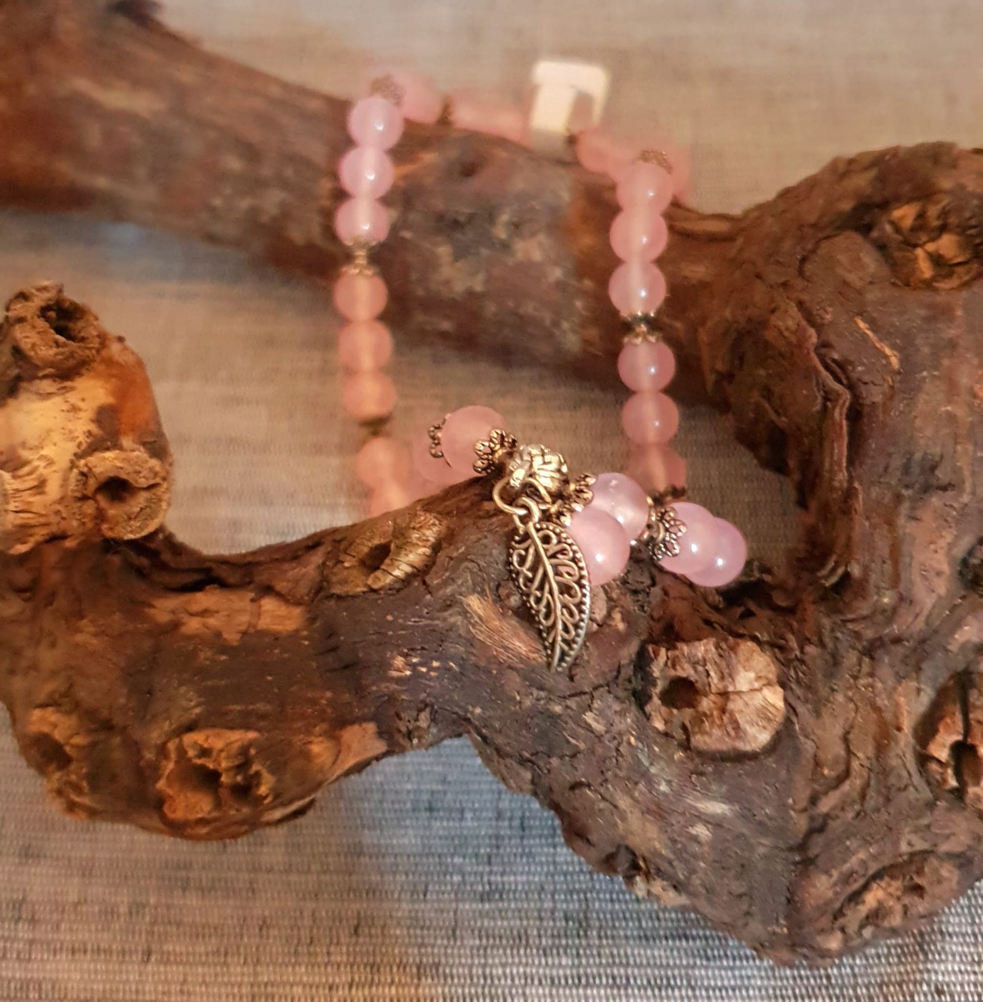 Bracelet de perles roses avec une breloque en forme de feuille d'argent posée sur du bois flotté texturé.