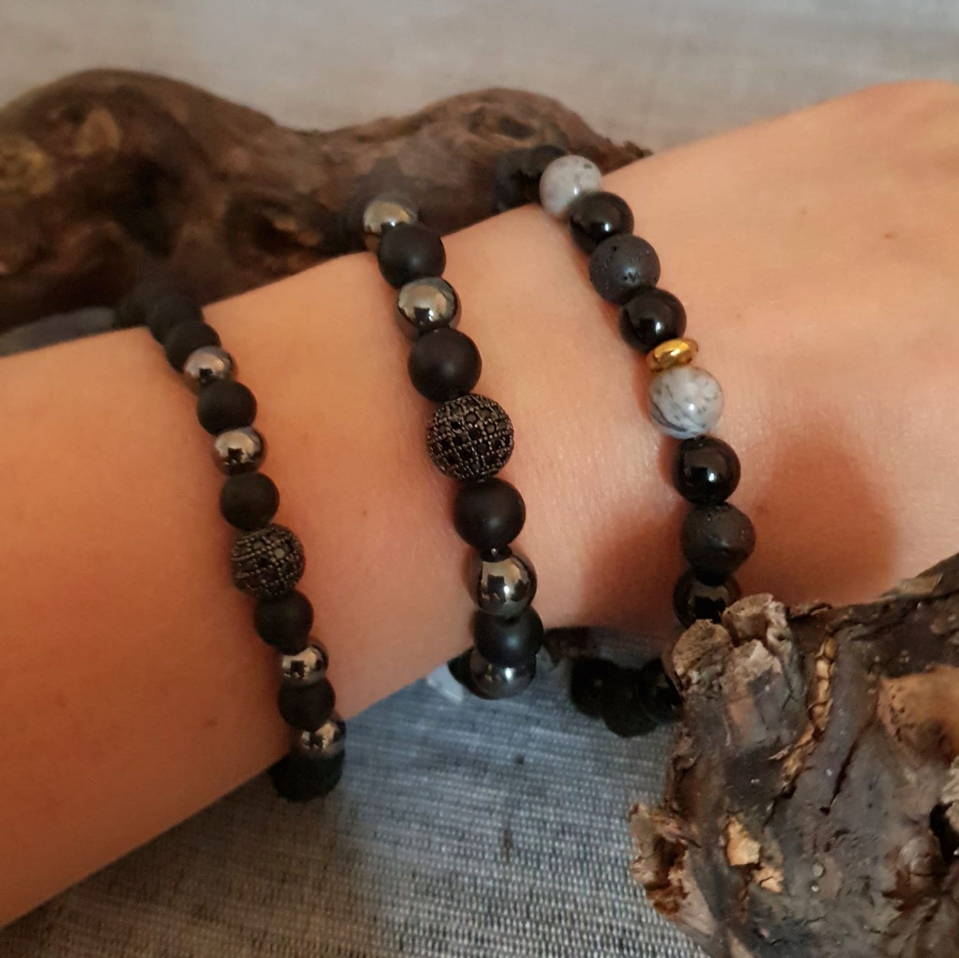 Trois bracelets de perles noires, grises et argentées sur un poignet, sur un fond texturé.