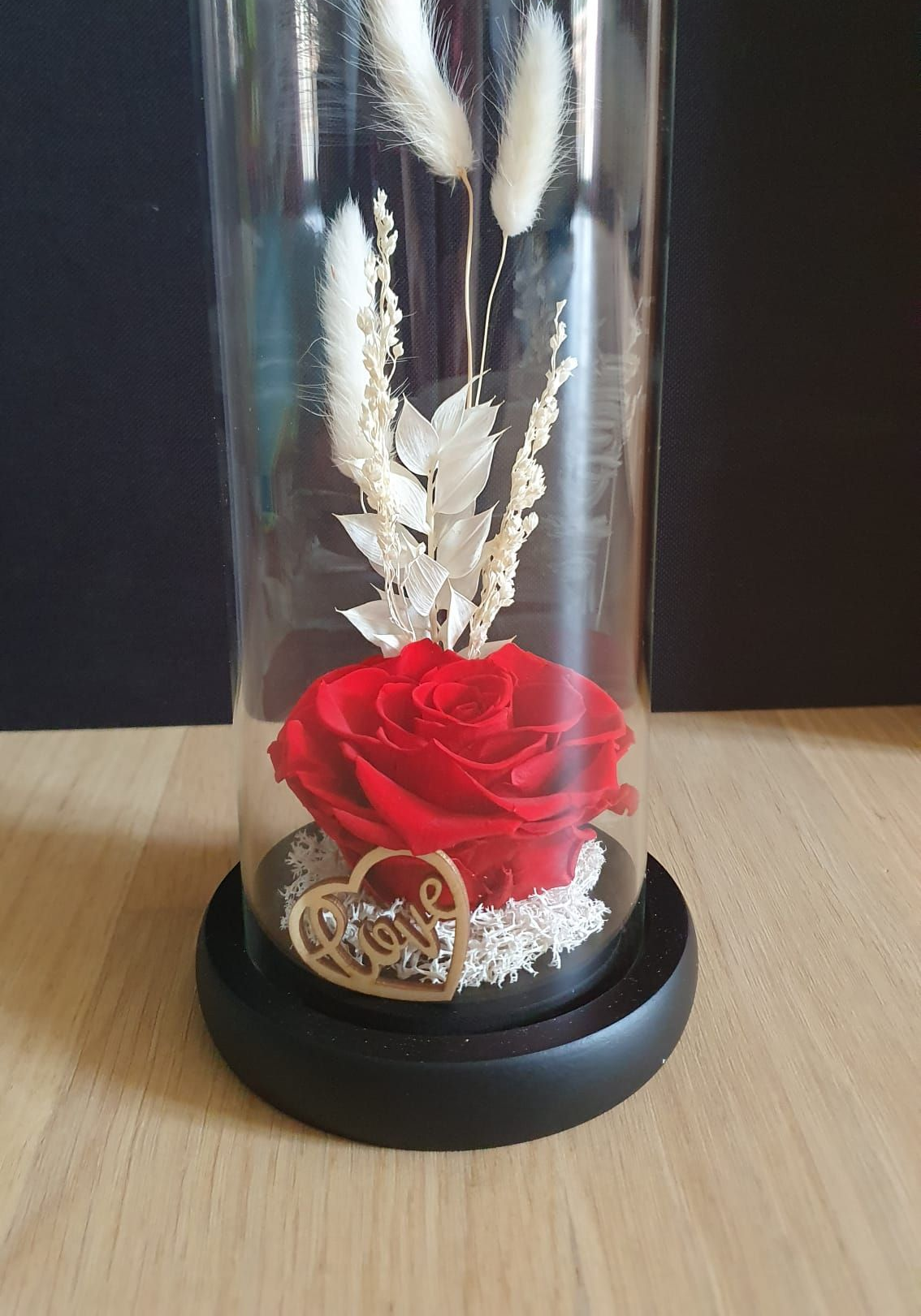 Rose rouge et fleurs blanches séchées sous cloche en verre sur un socle noir